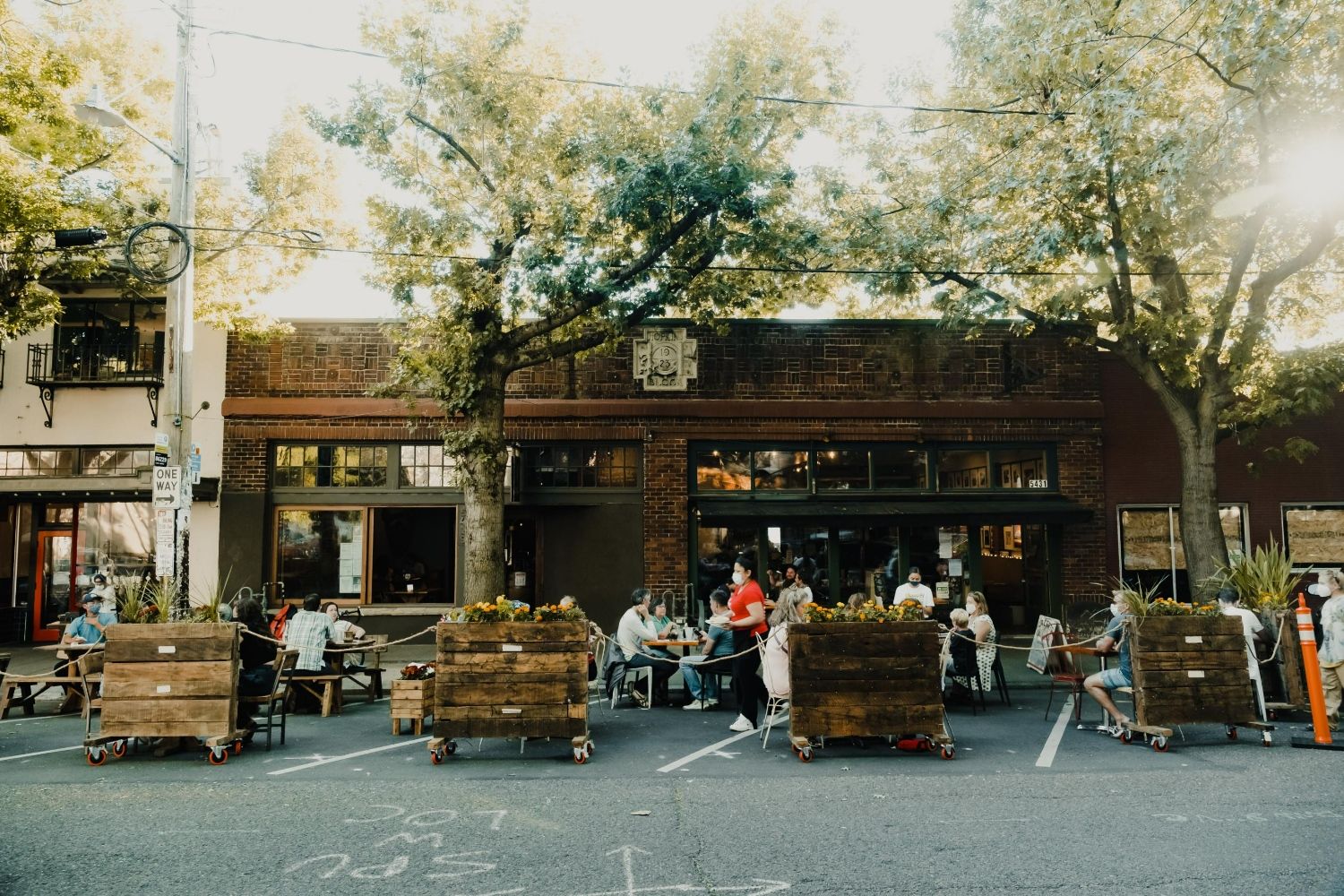 Outdoor seating area with patrons at a restaurant surrounded by wooden planters.