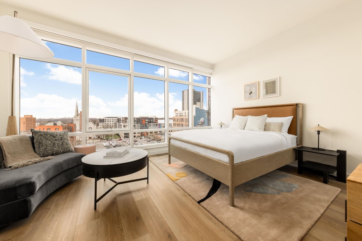 Bright modern bedroom with a bed, sofa, and large window overlooking the city.