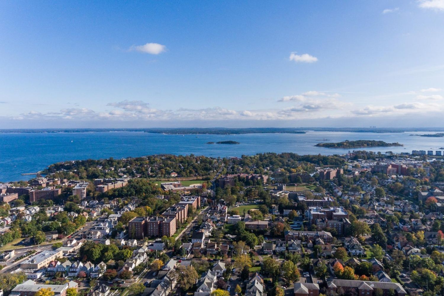 Aerial view of a coastal town with buildings and a blue lake under a clear sky.