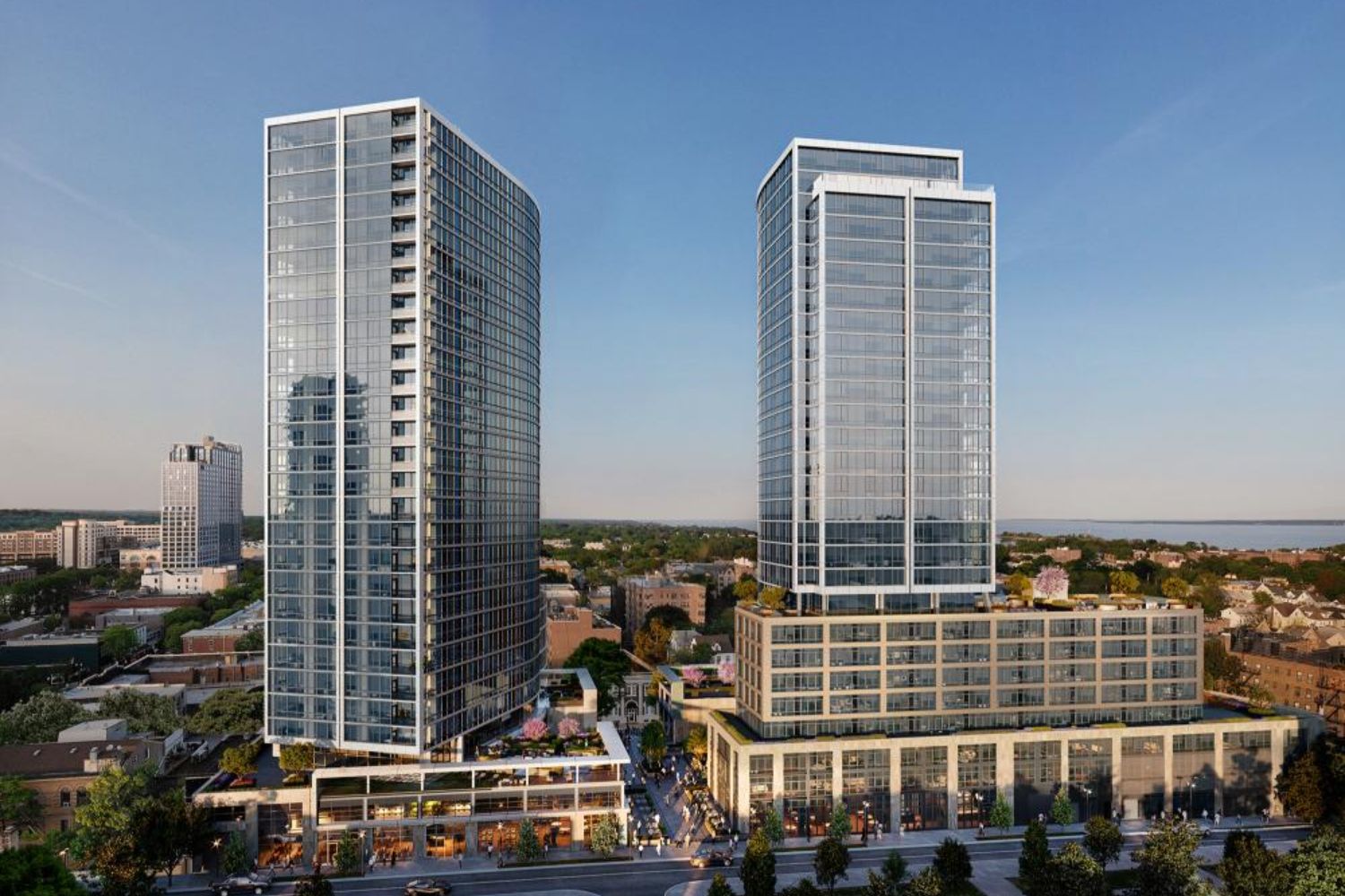 Two modern, glass skyscrapers with a mixed-use base in an urban setting.