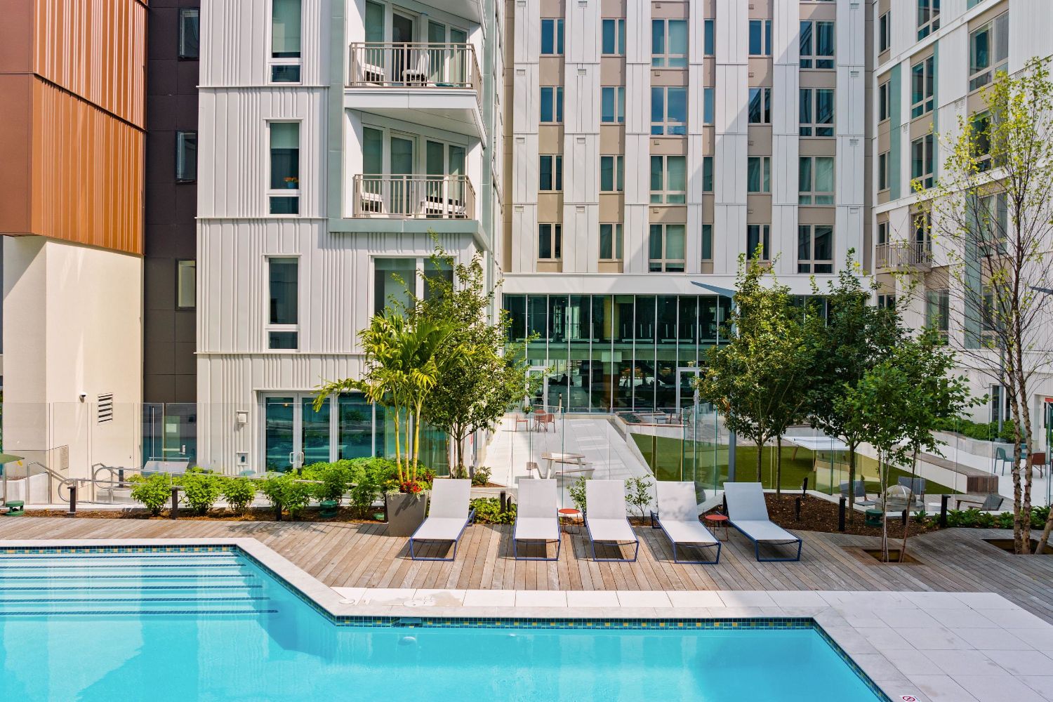 Modern pool area with lounge chairs and surrounding greenery in an apartment complex.