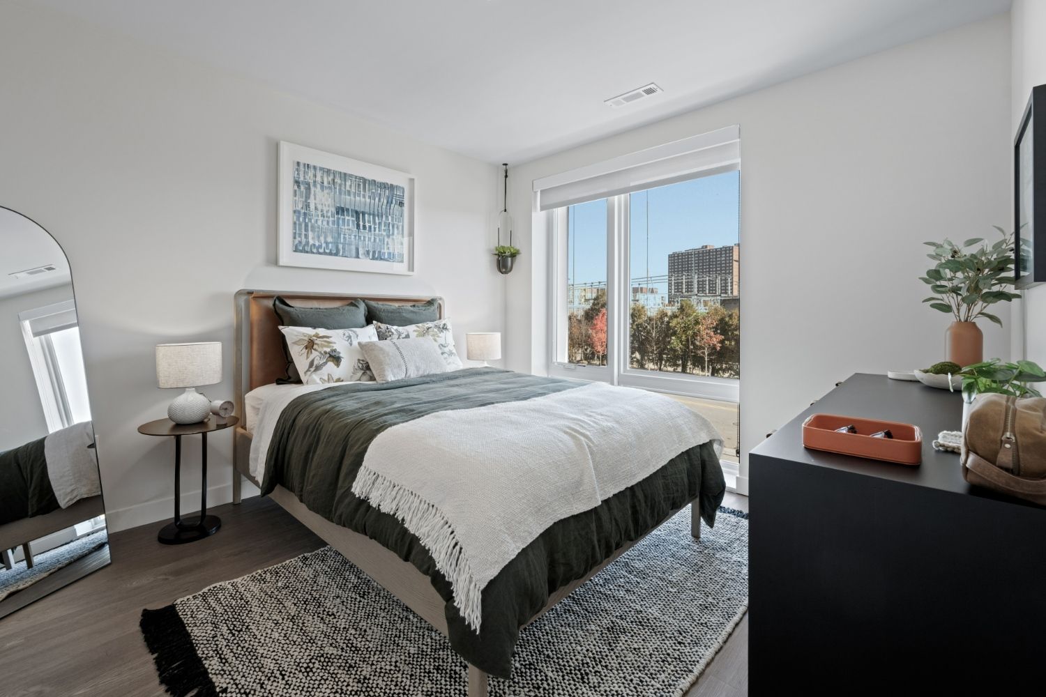 Bright bedroom with alrge windwo, green bedding, wall art and full-length mirror