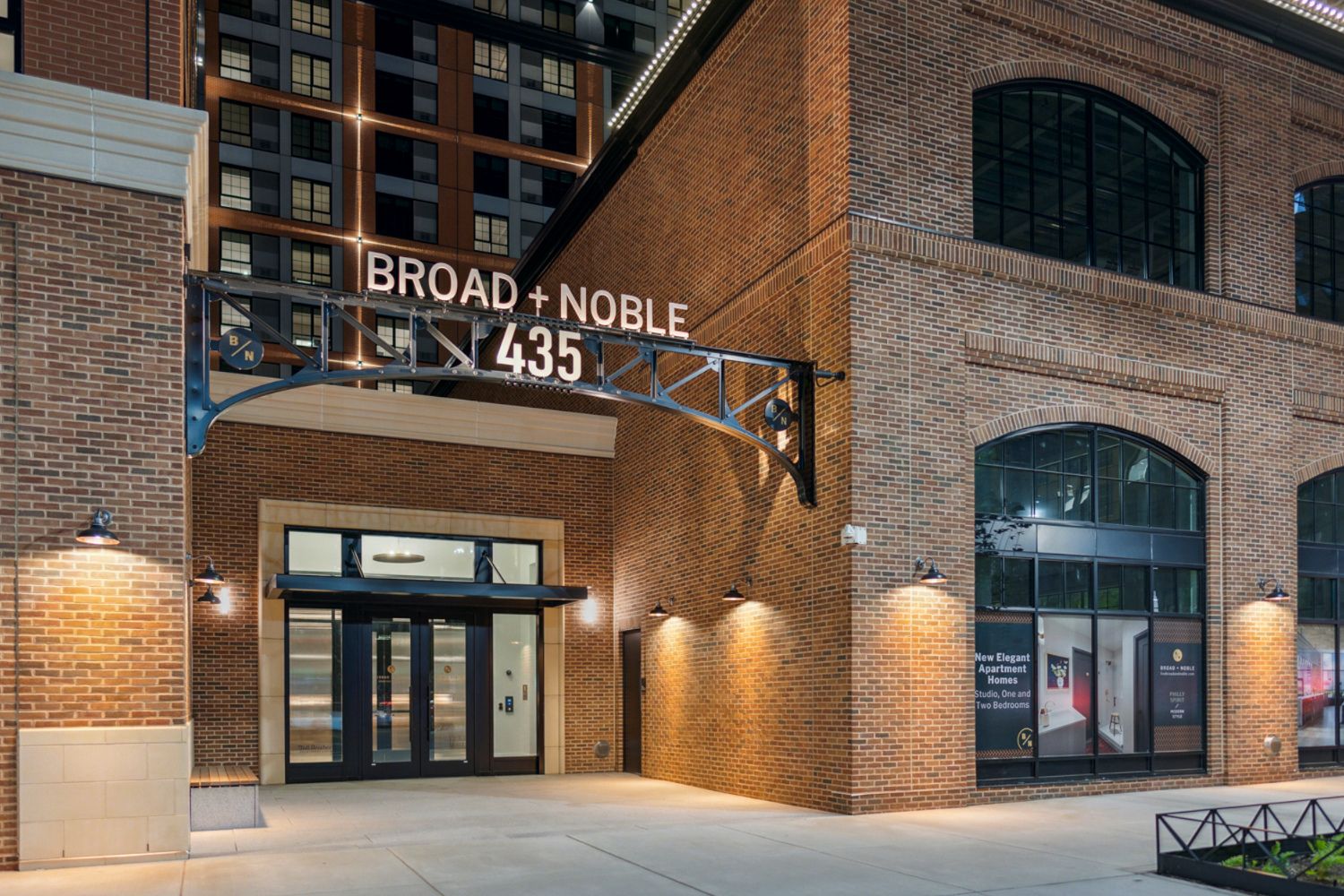 Broad + Noble 435 brick building entrance with large sign and lit storefront windows
