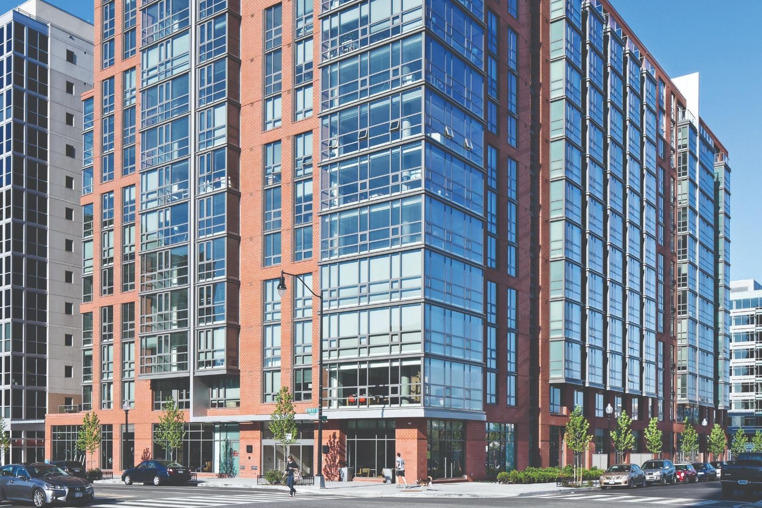 Modern mid-rise apartment building with red brick and large glass windows on city street