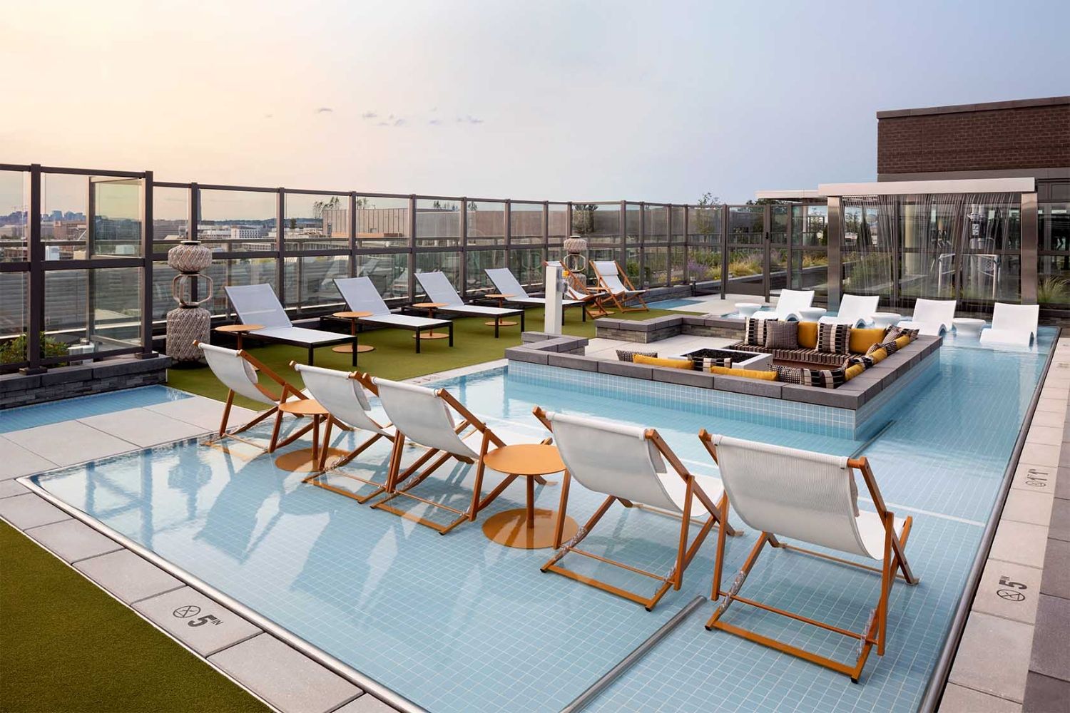 Rooftop pool with in-water lounge chairs, cabana seating, and turf sun deck at sunset