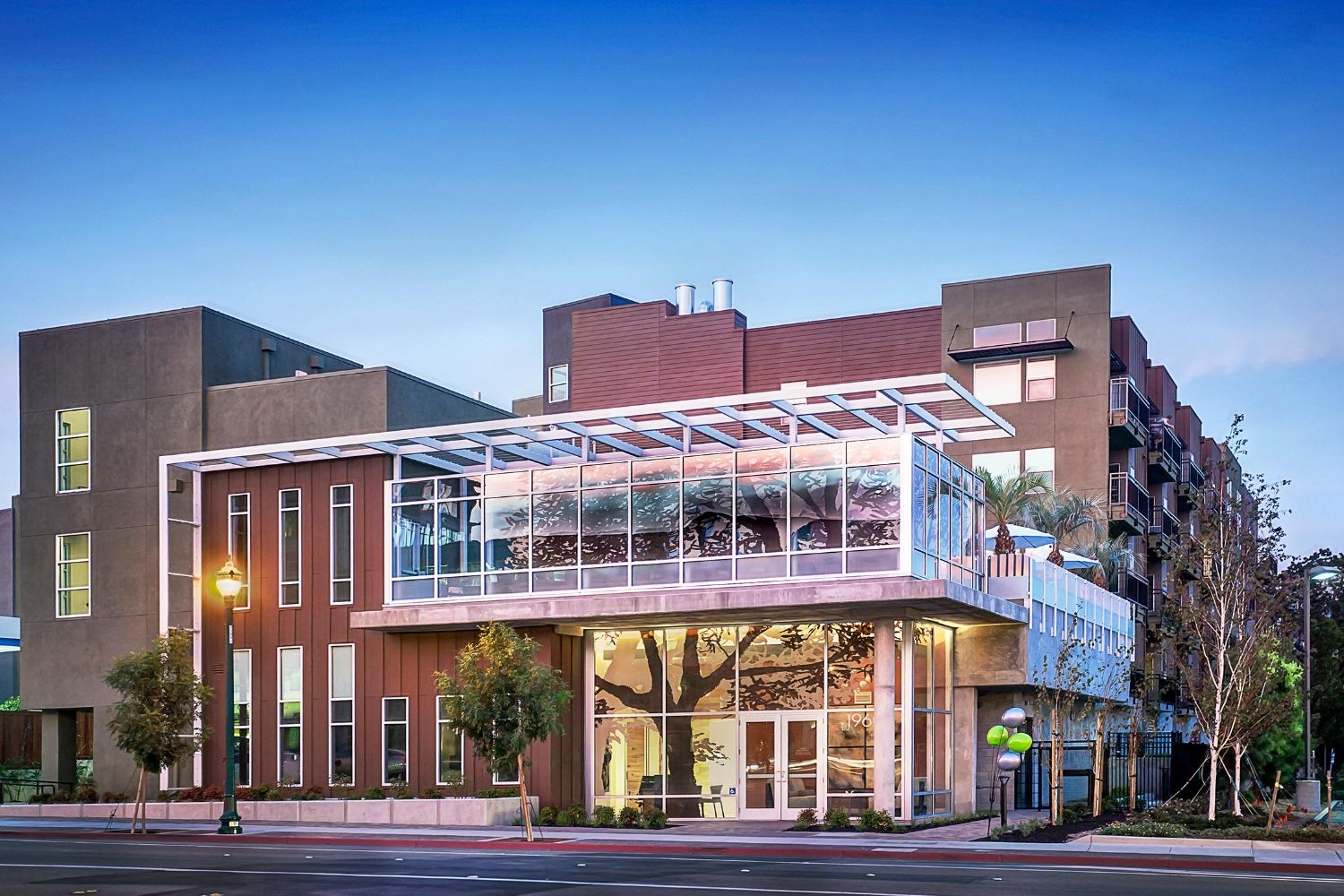Modern multi-story building with a glass entrance and surrounding trees.