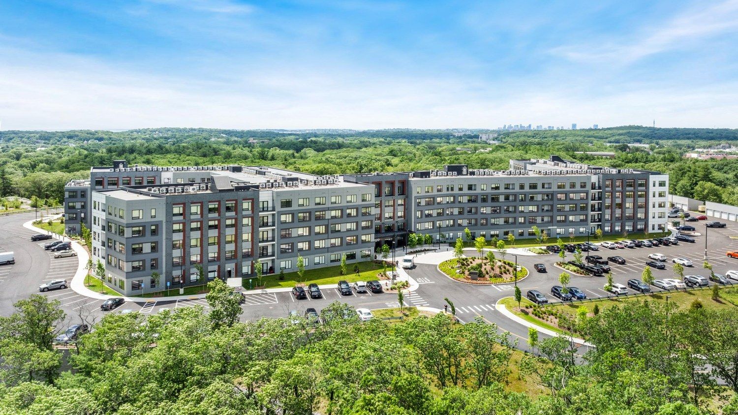 Modern apartment complex surrounded by green landscape and parking area.