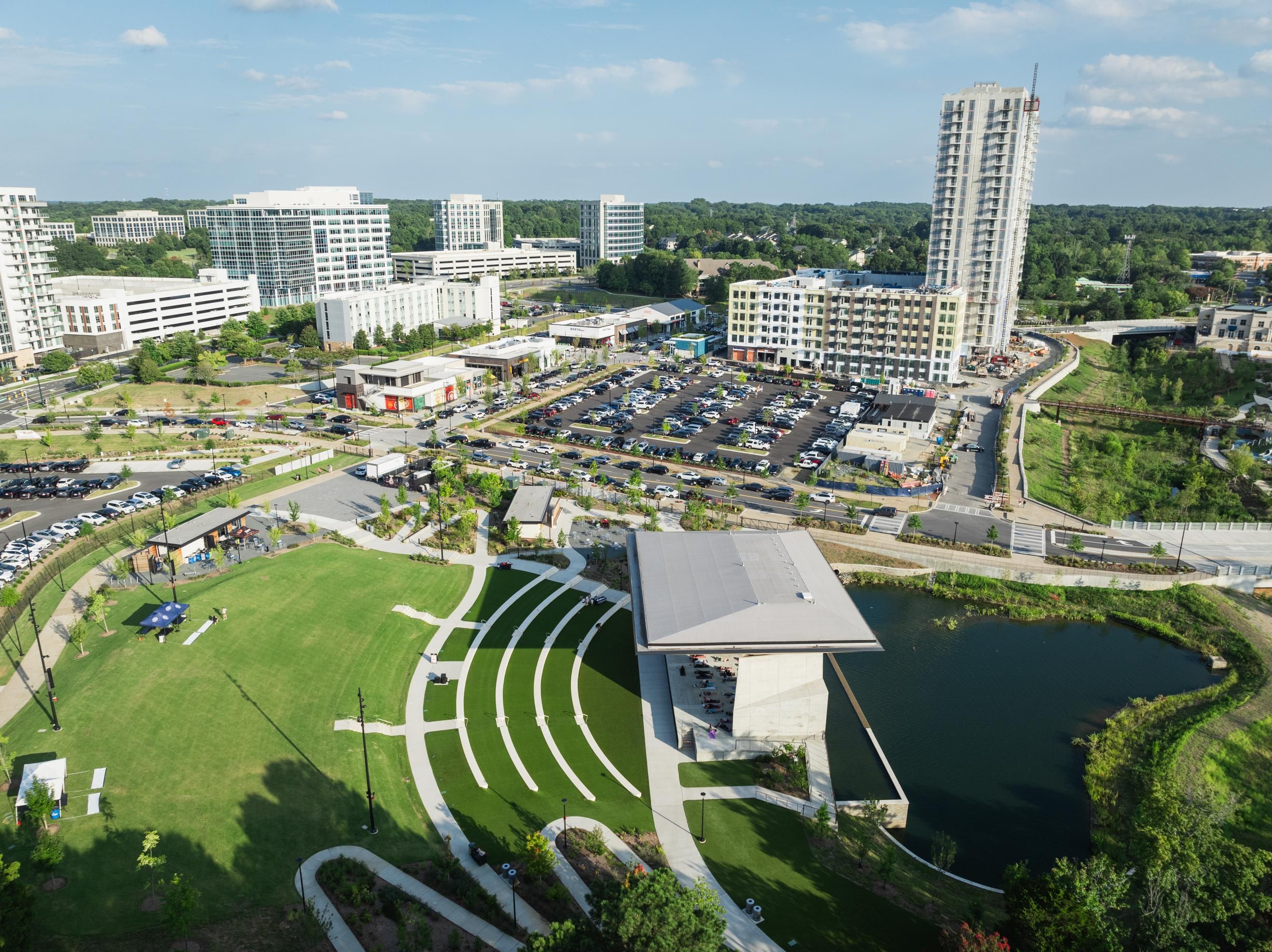 Aerial view of a modern urban area with buildings, green spaces, and a pond.