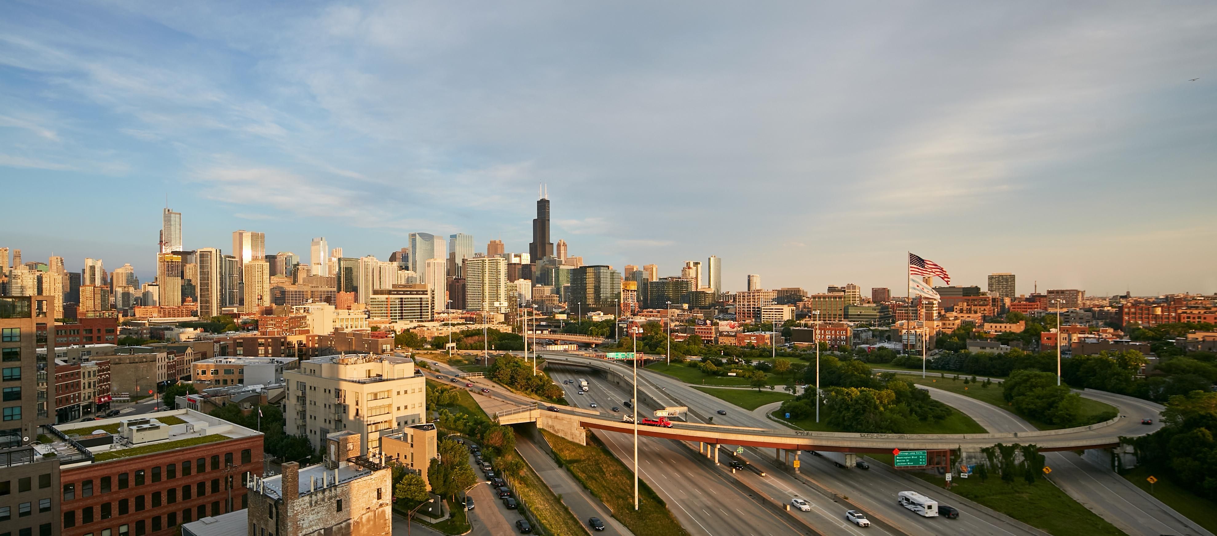 Panoramic view of a city skyline with highways and greenery under a clear sky.