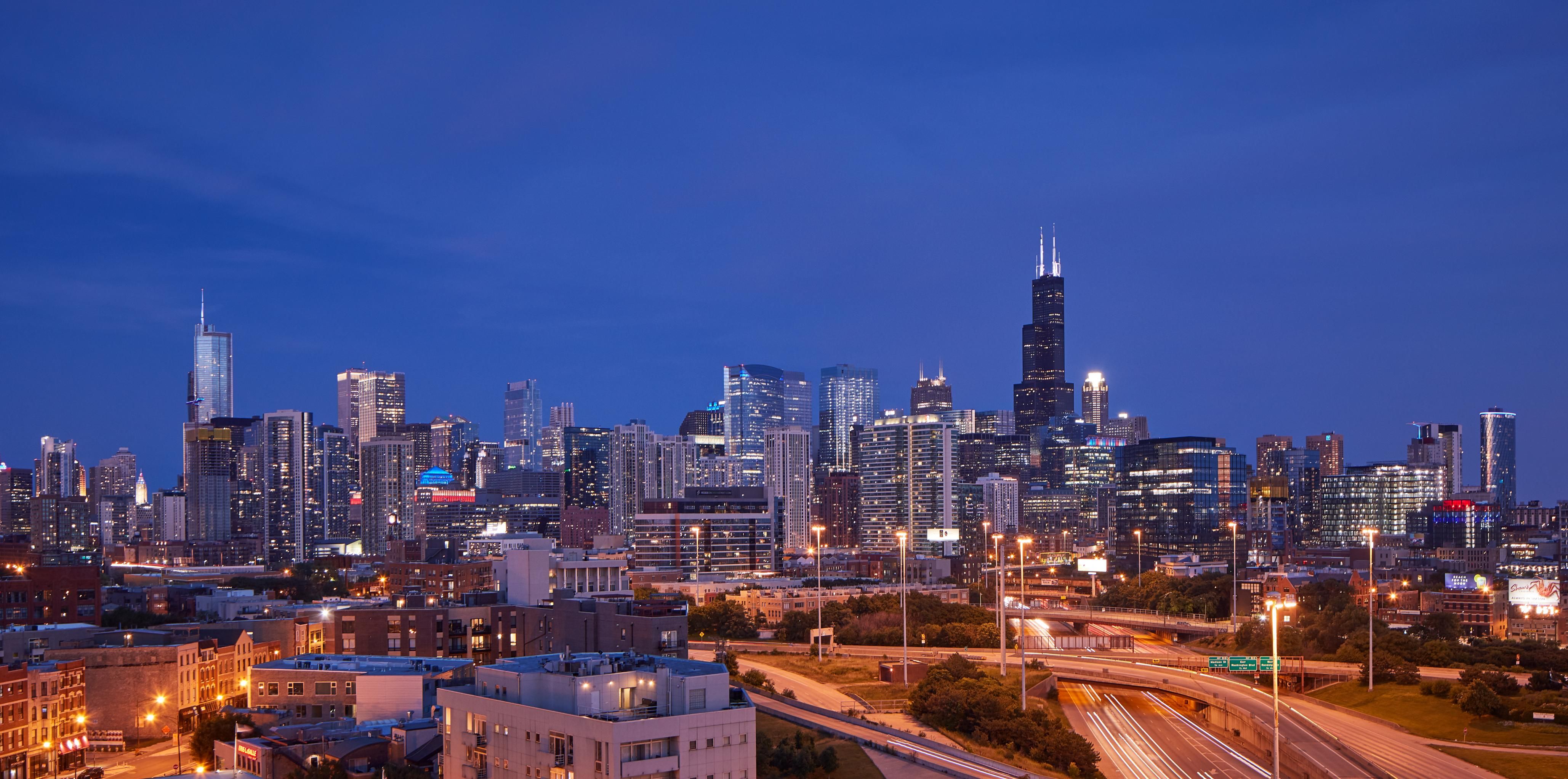 Chicago skyline at dusk with illuminated buildings and highways.