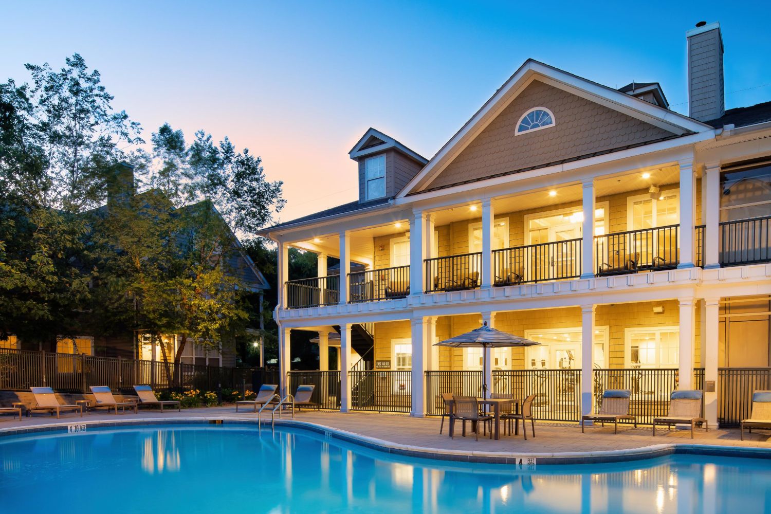 A serene pool and elegant two-story house surrounded by trees at twilight.