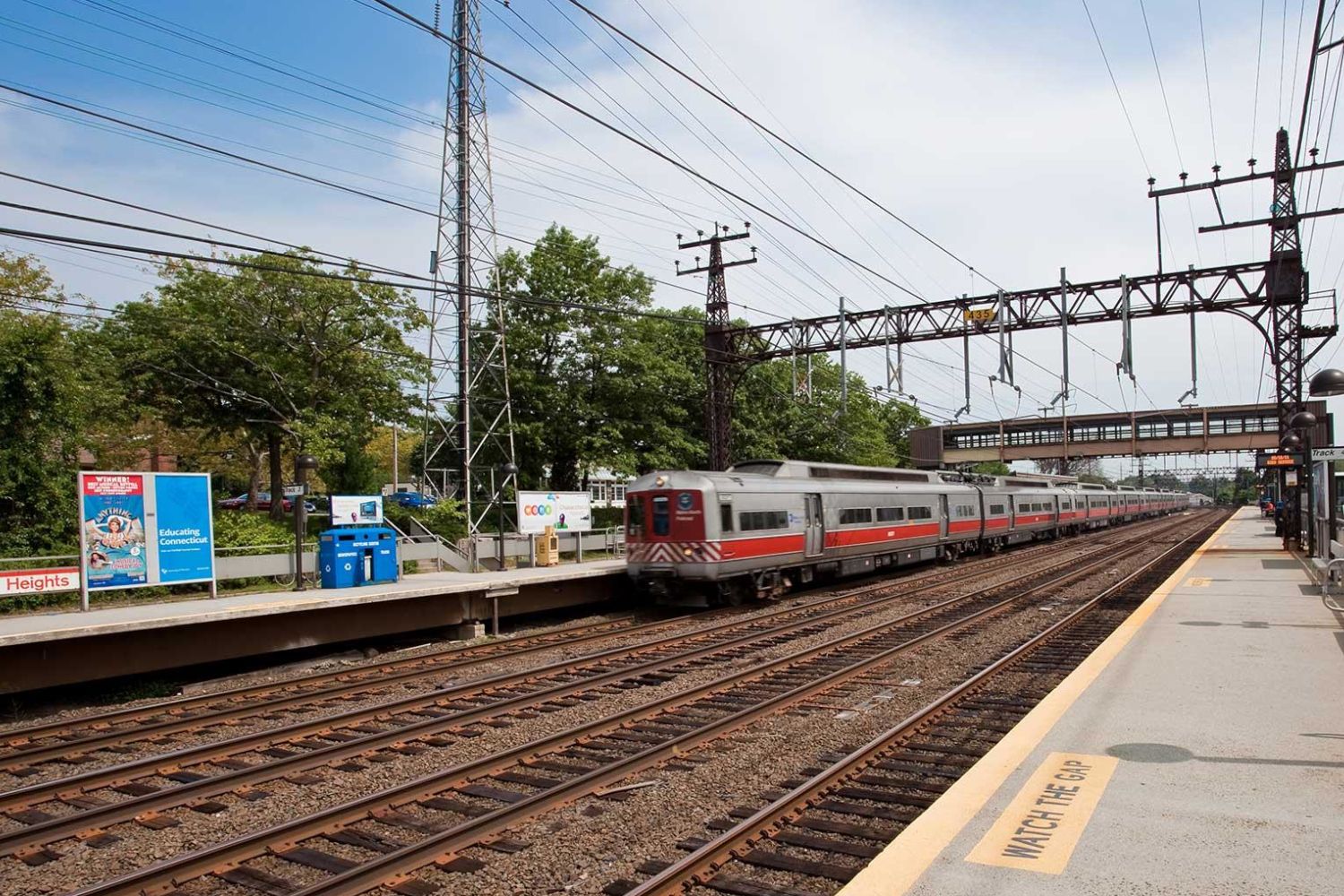 Train approaching a station with platforms and power lines in the background.