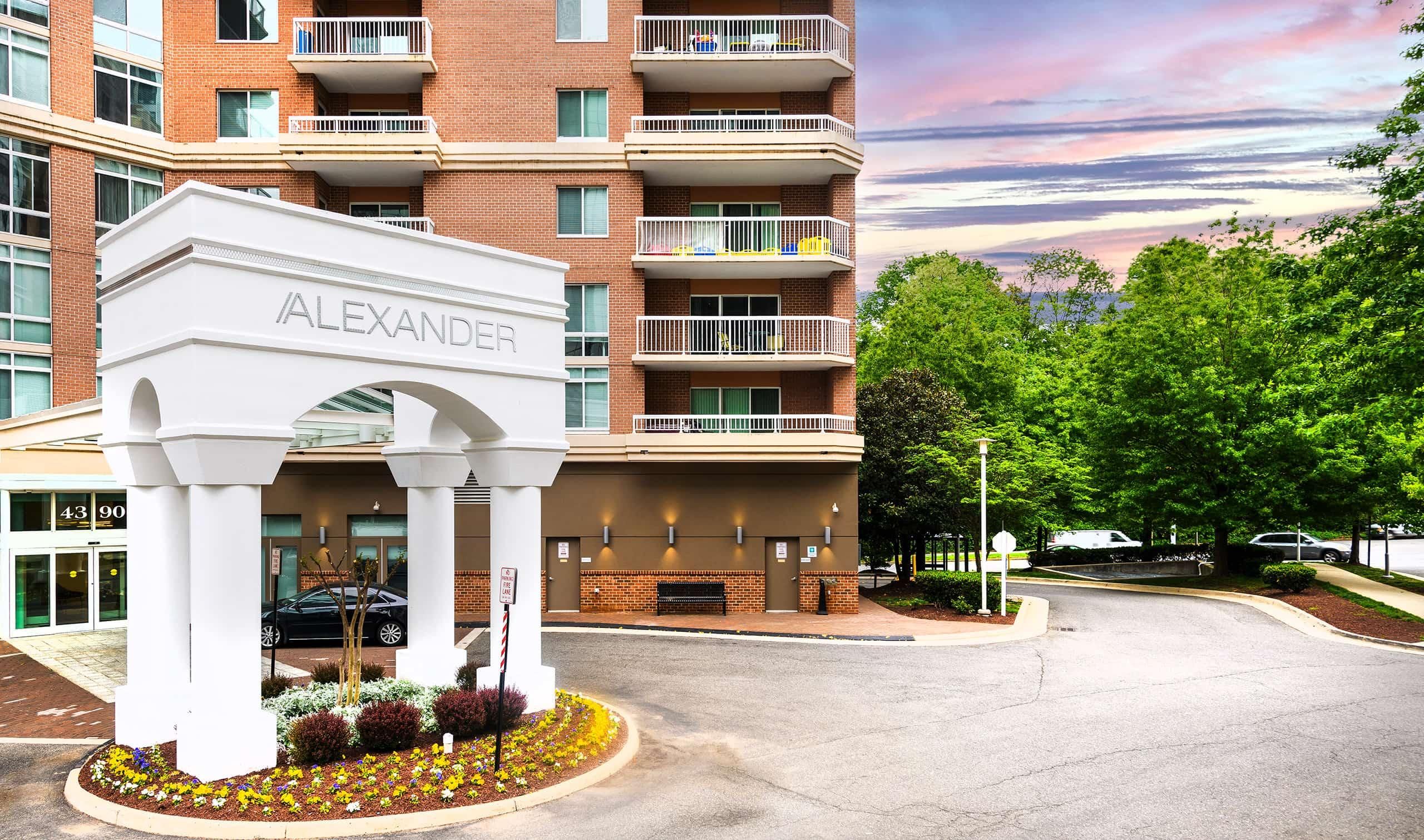 Modern building entrance with "Alexander" sign and landscaped surroundings.