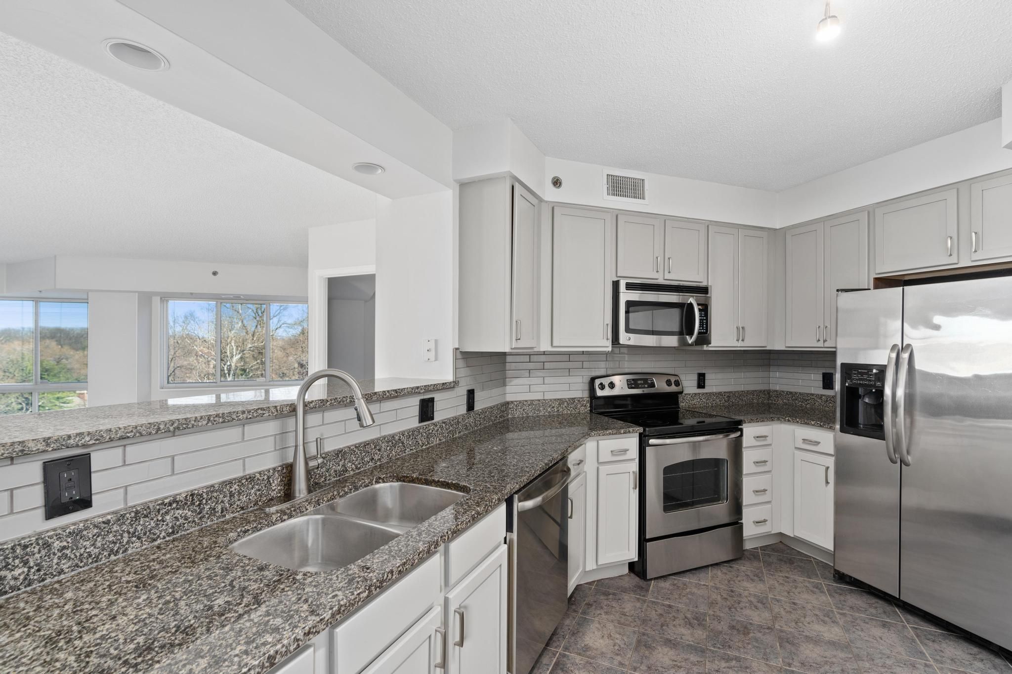 Modern kitchen with gray cabinets, granite countertops, and stainless steel appliances.