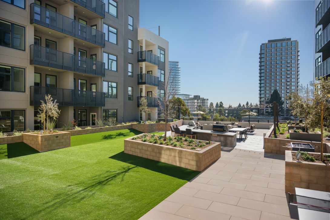 Modern apartment complex with landscaped garden and seating area under clear blue sky.