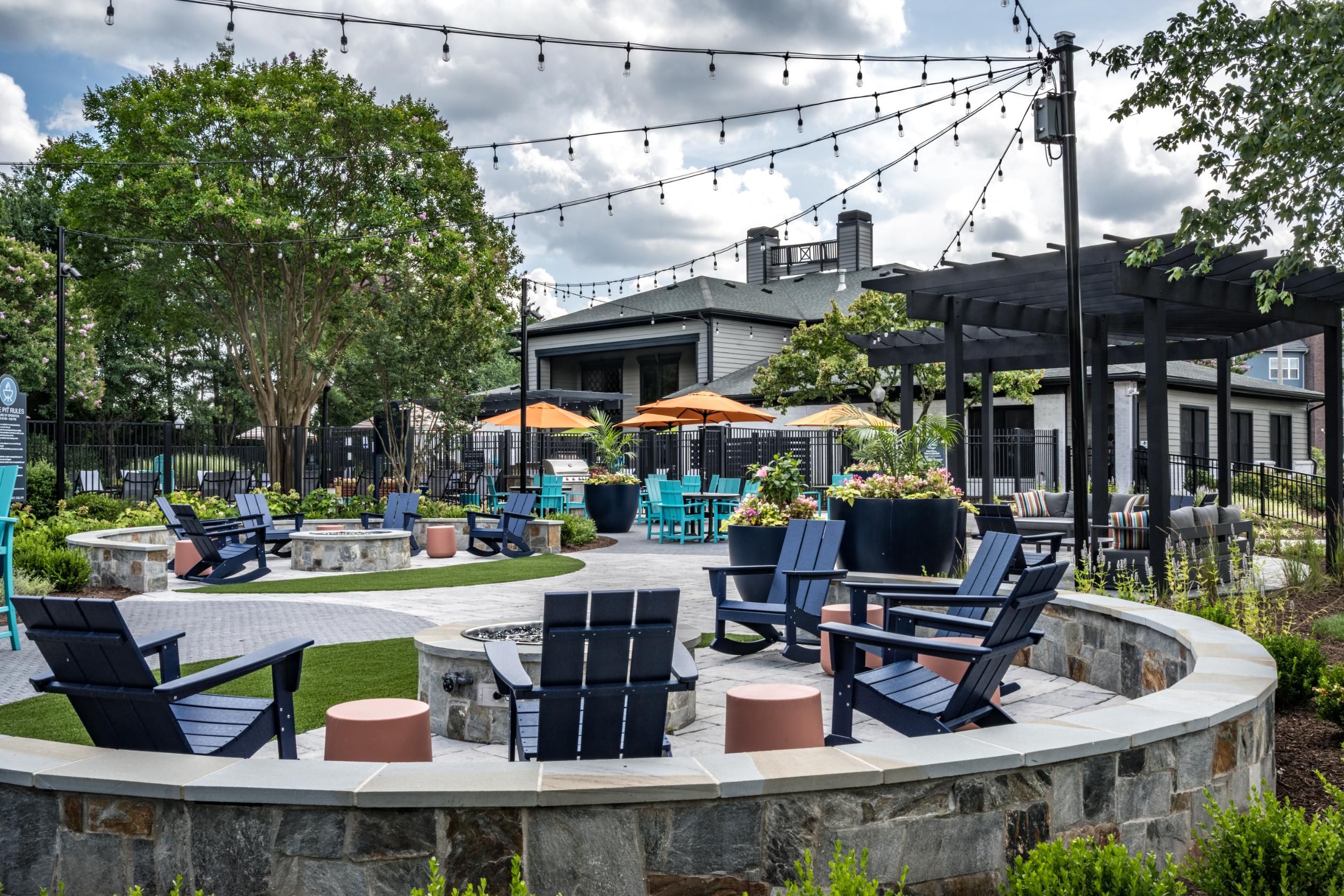 Cozy outdoor seating area with chairs and umbrellas, surrounded by greenery and string lights.