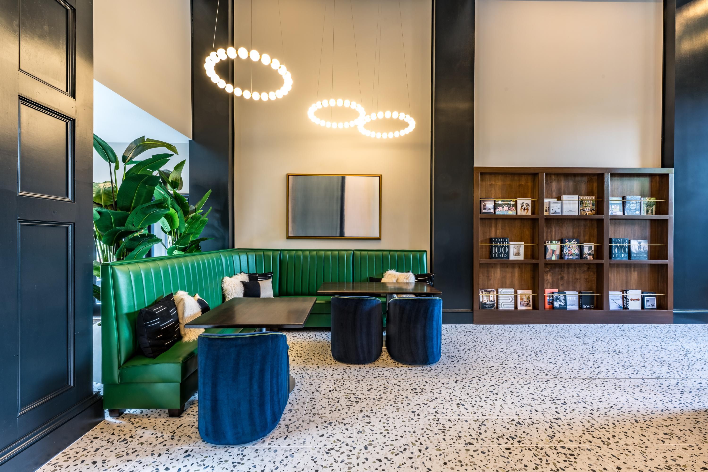 Modern lounge with green seating, round lights, and wooden shelves filled with books.