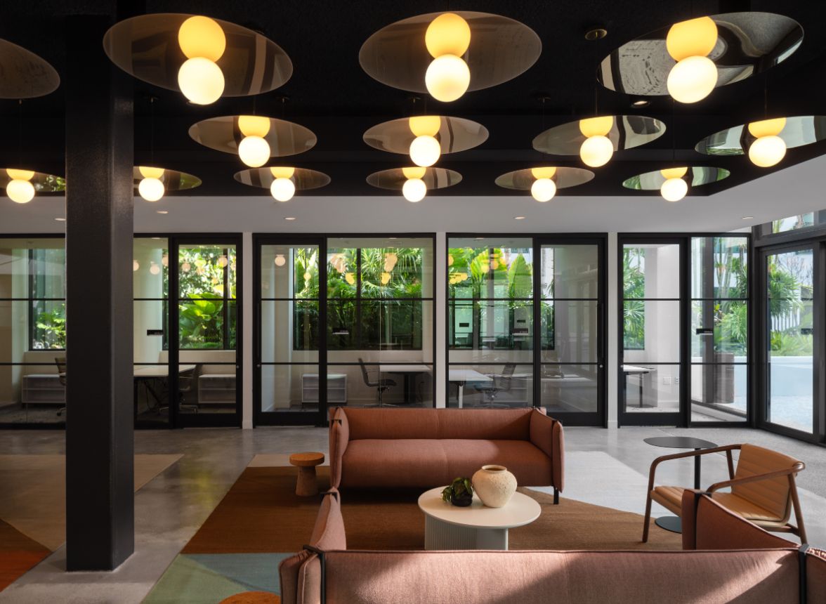 Modern lounge with circular light fixtures, sofas, and large glass windows revealing greenery.