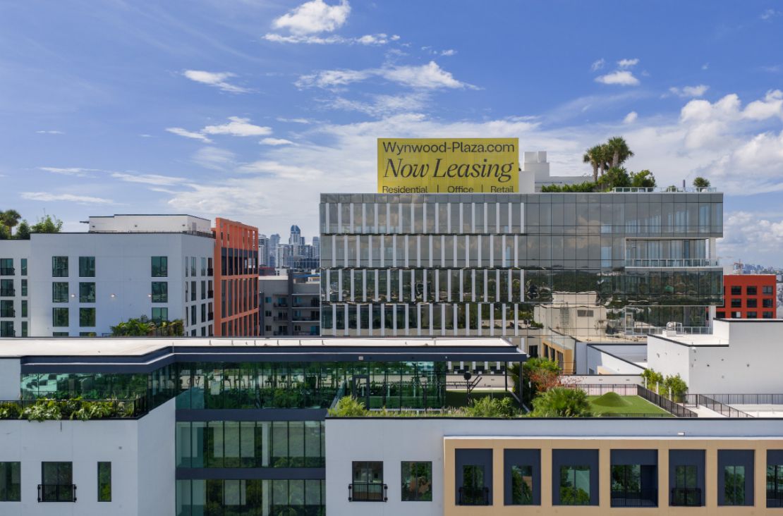 Modern building with a prominent yellow leasing sign against a blue sky.