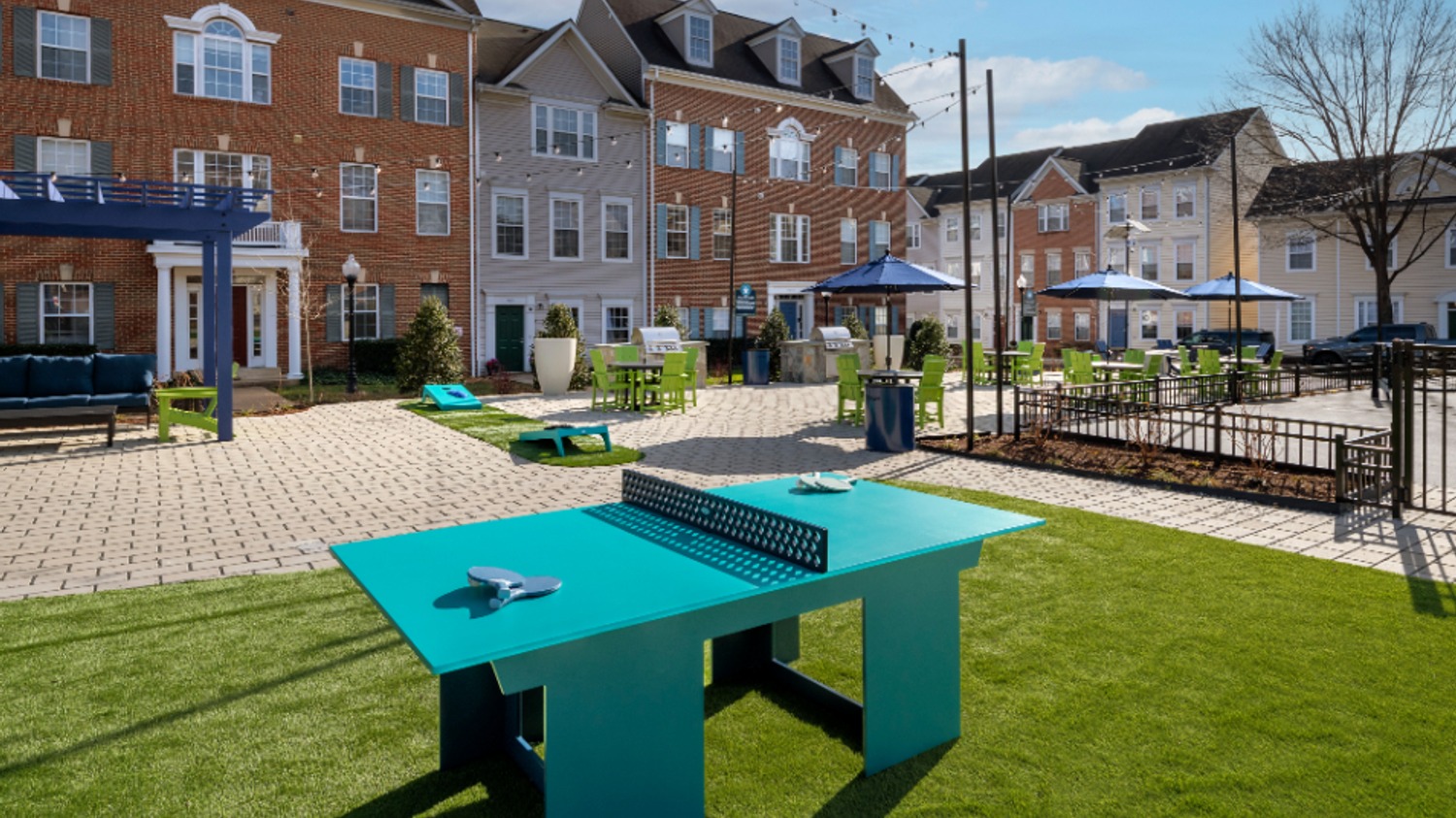 Outdoor space featuring a ping pong table and seating, with buildings in the background.