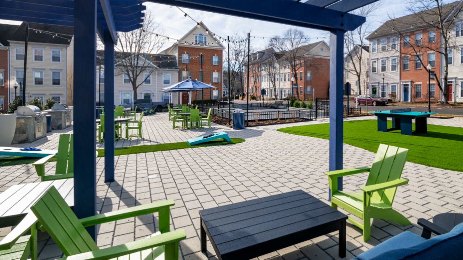 Outdoor communal space with green chairs, tables, and buildings in the background.