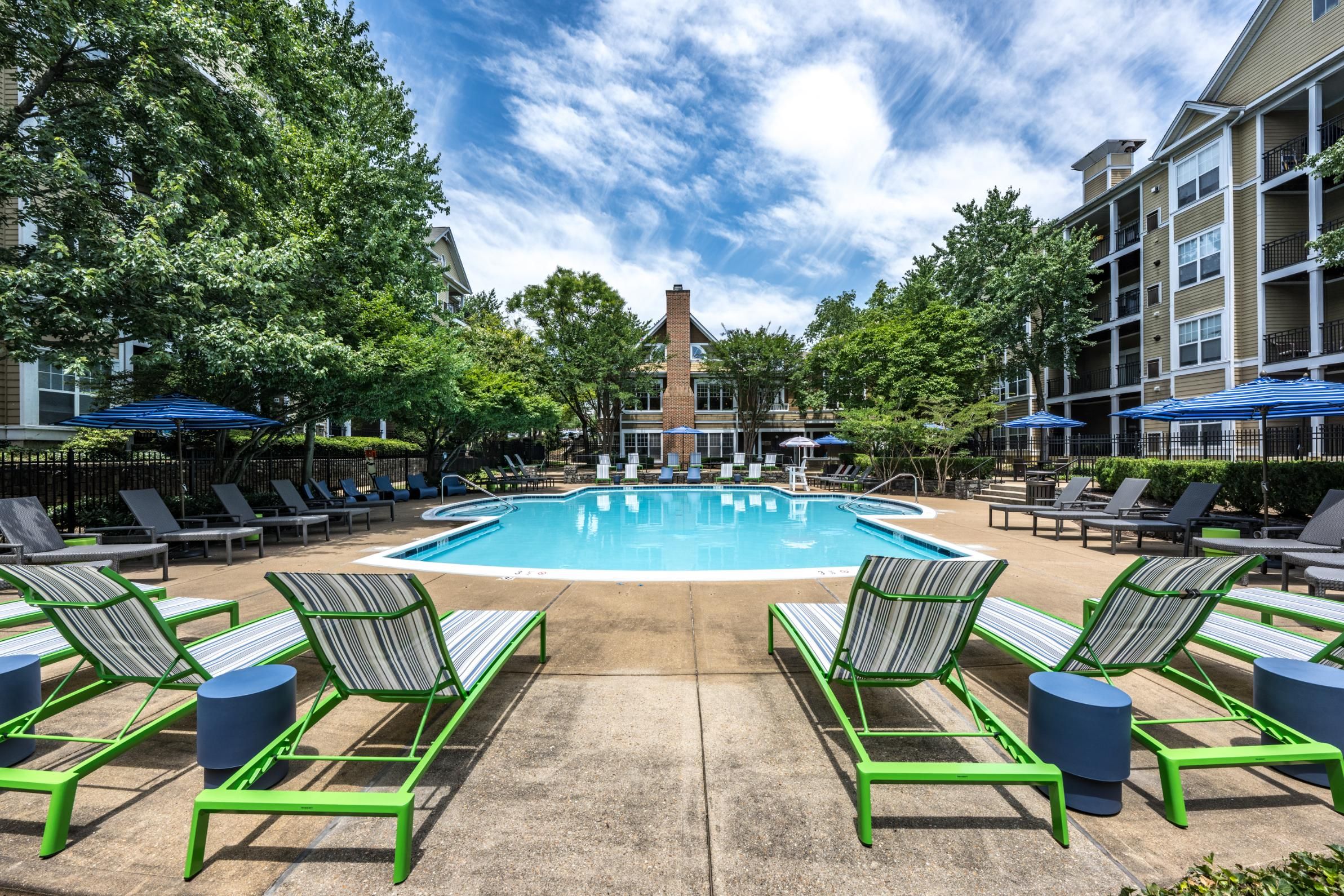 A serene pool area surrounded by lounge chairs and trees under a blue sky.
