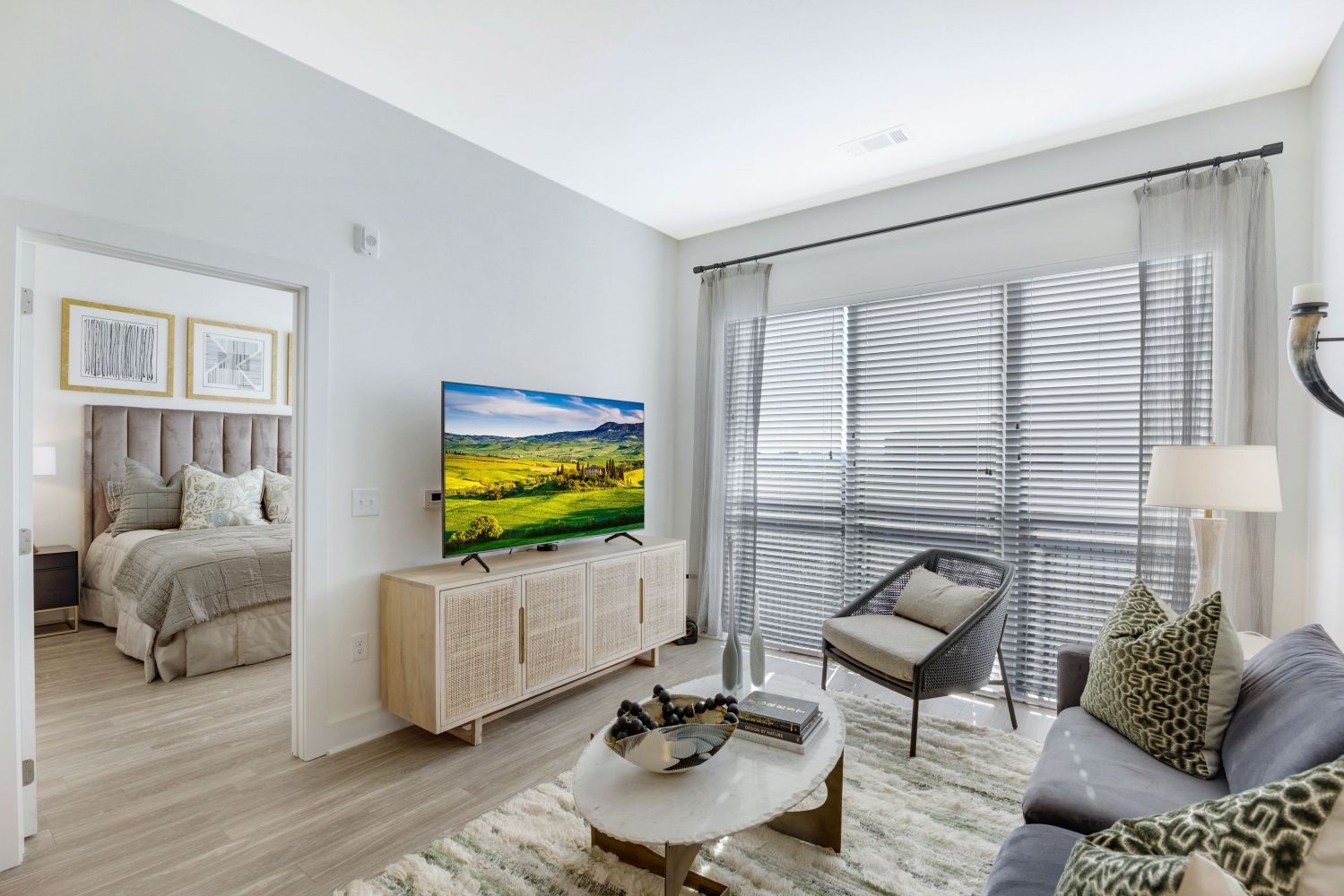 Modern living room with a TV, sofa, and window, leading to a bedroom.