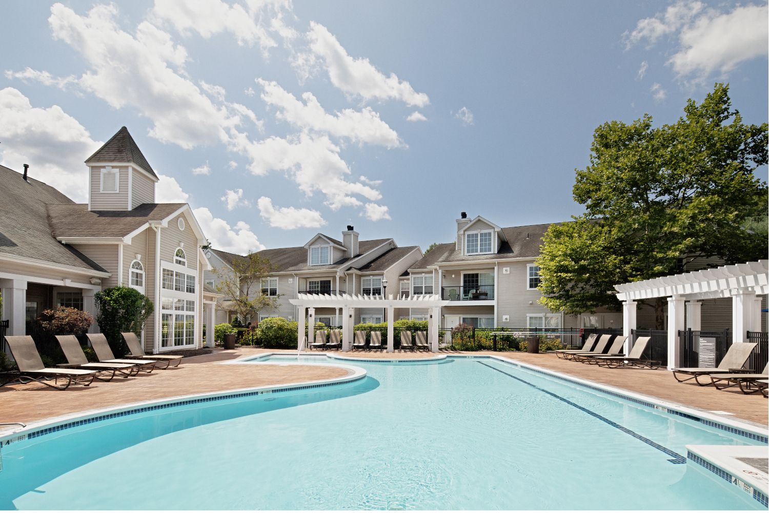 A serene pool area surrounded by lounge chairs and buildings under a clear blue sky.