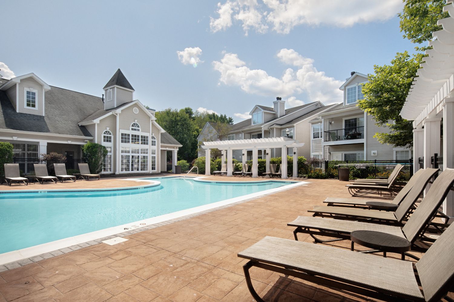 Pool area with lounge chairs and nearby buildings under a partly cloudy sky.