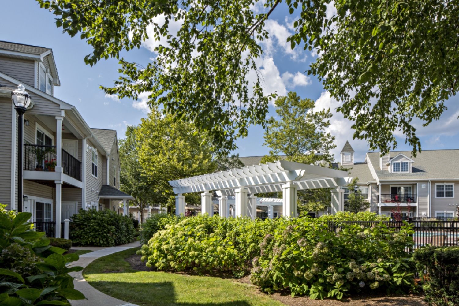A landscaped area with a pergola between modern buildings under a blue sky.
