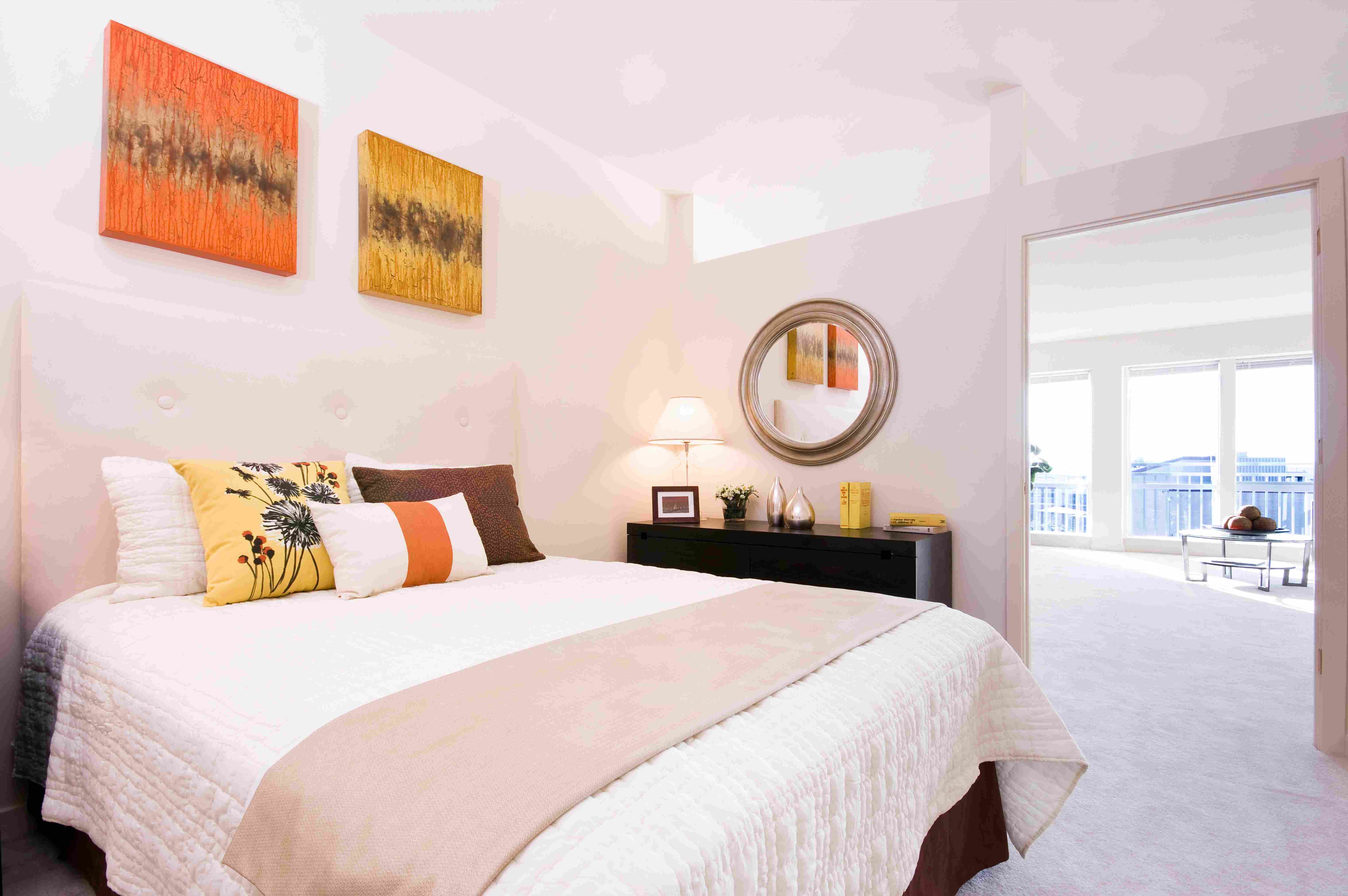Bright bedroom with a large bed, colorful wall art, and a view through an open doorway.