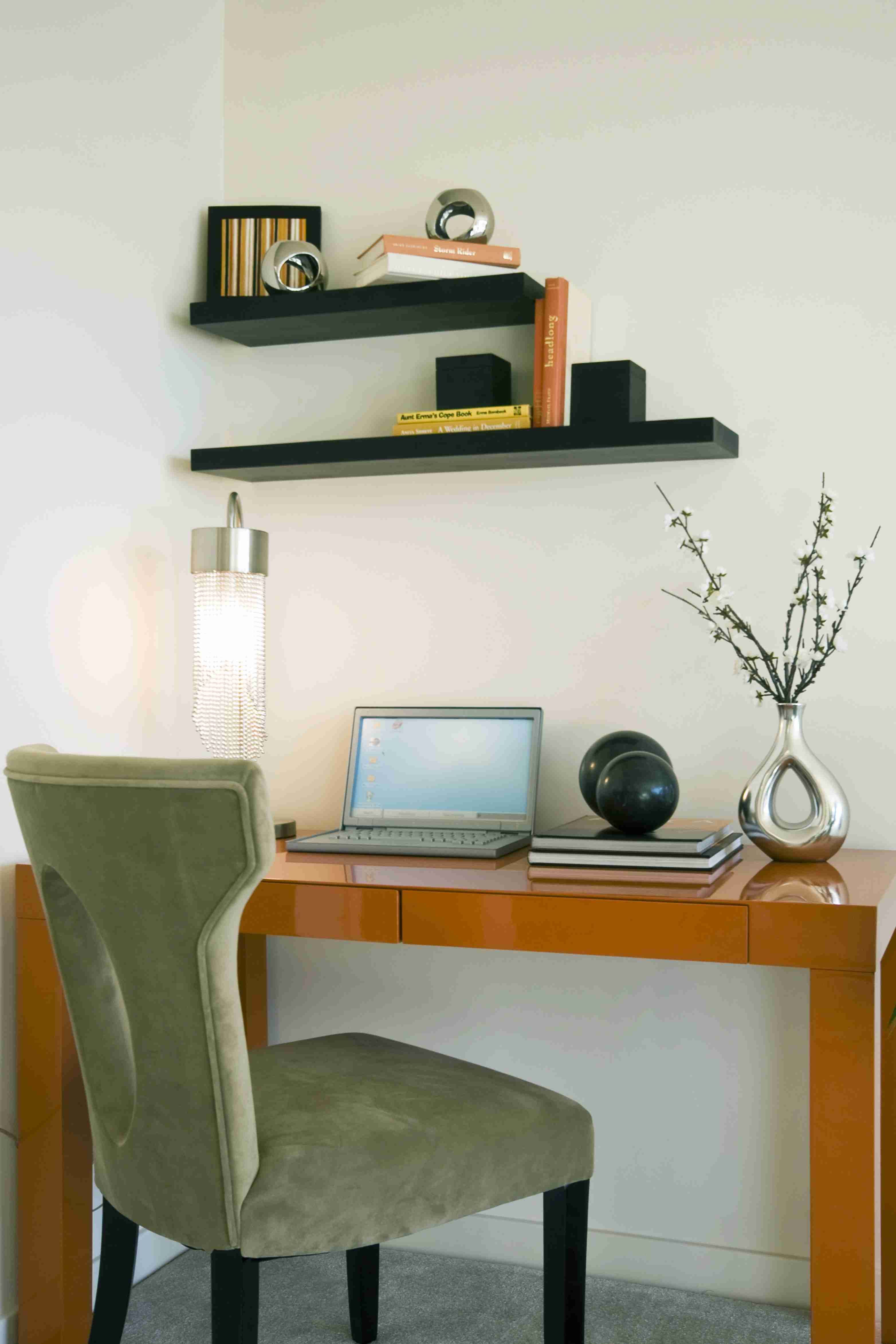 A minimalist workspace with a desk, chair, laptop, and decorative shelves.