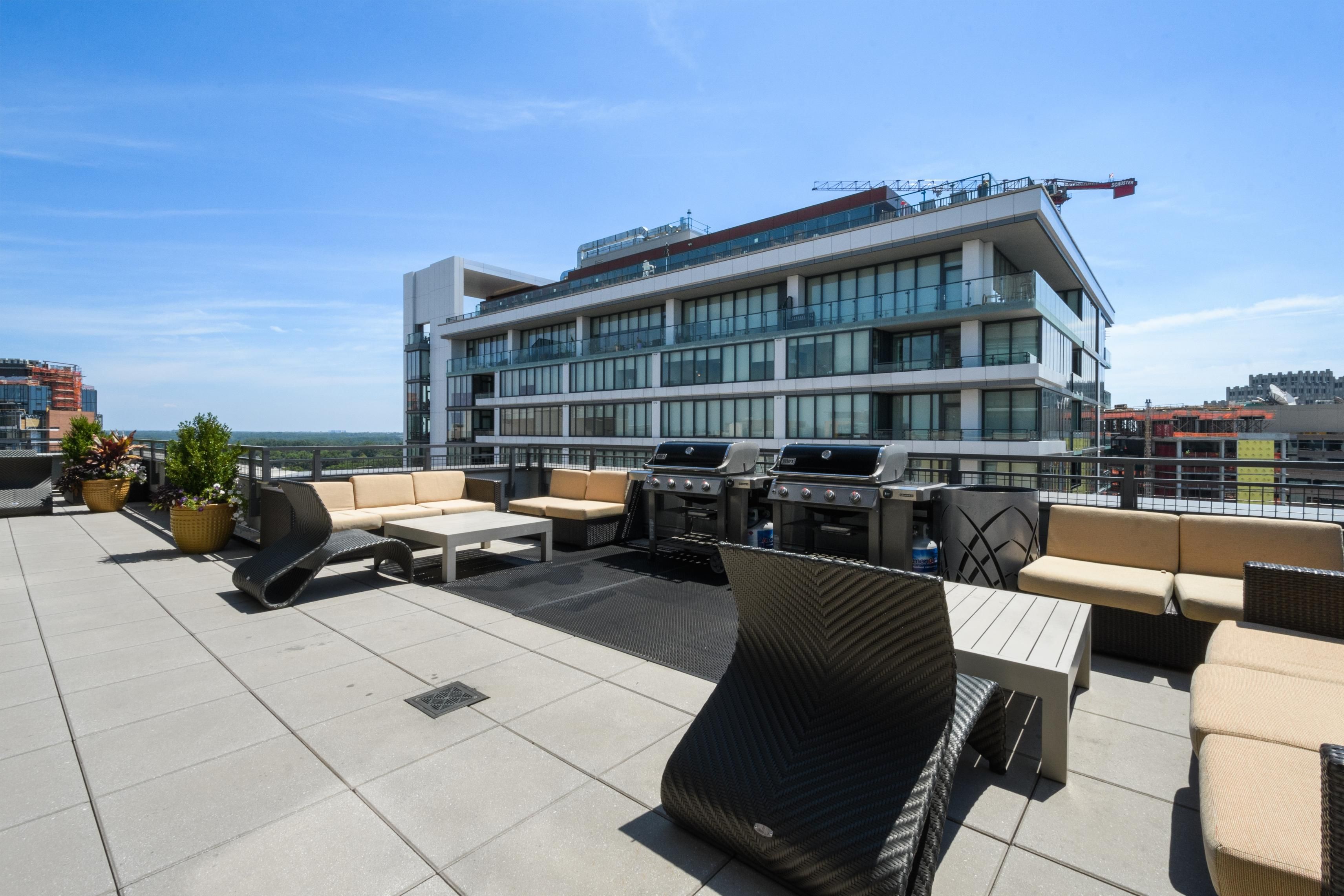 Rooftop terrace with seating and grills, overlooking a modern cityscape.