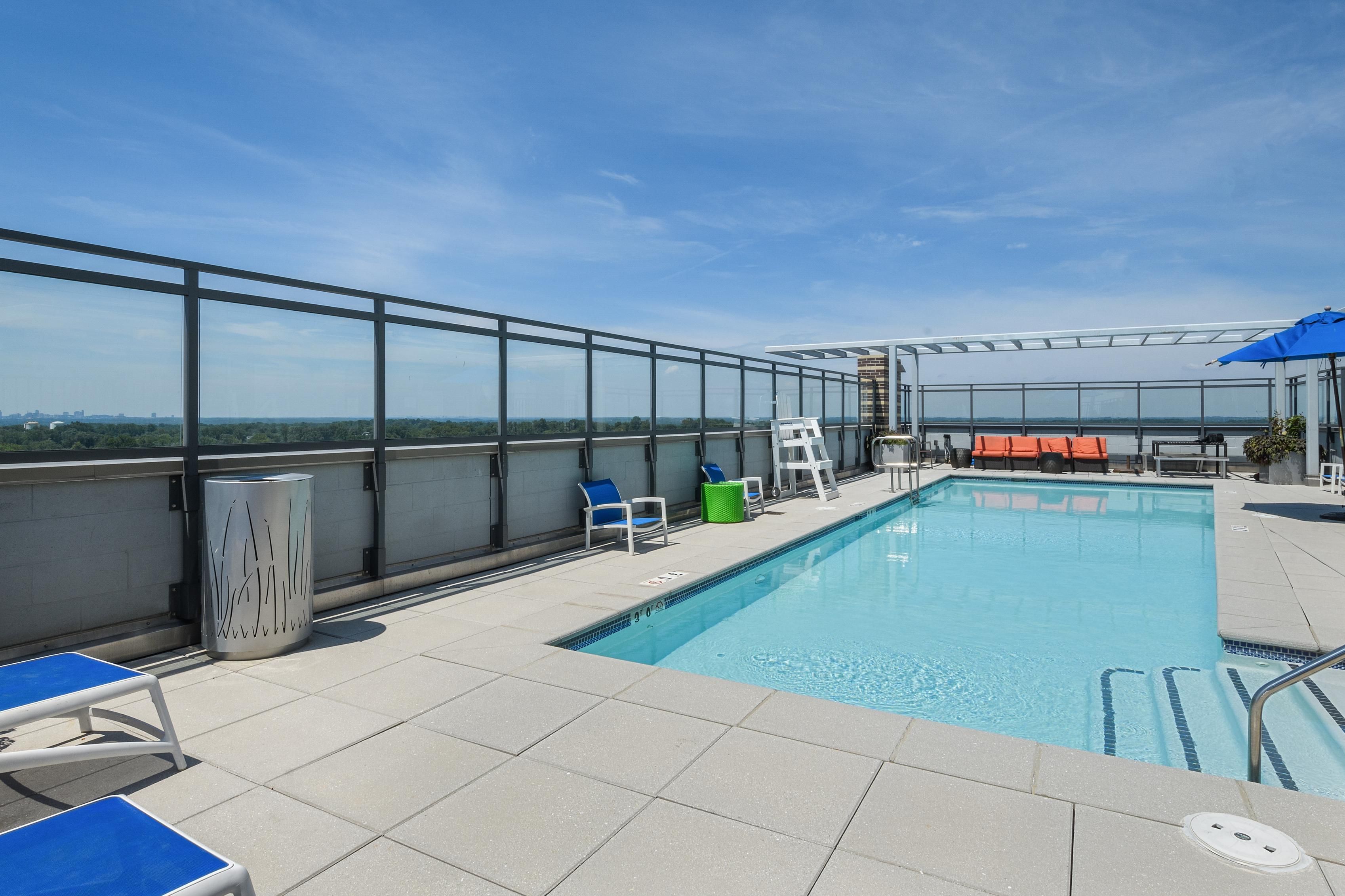 Rooftop pool area with blue sky, lounge chairs, and a panoramic view.
