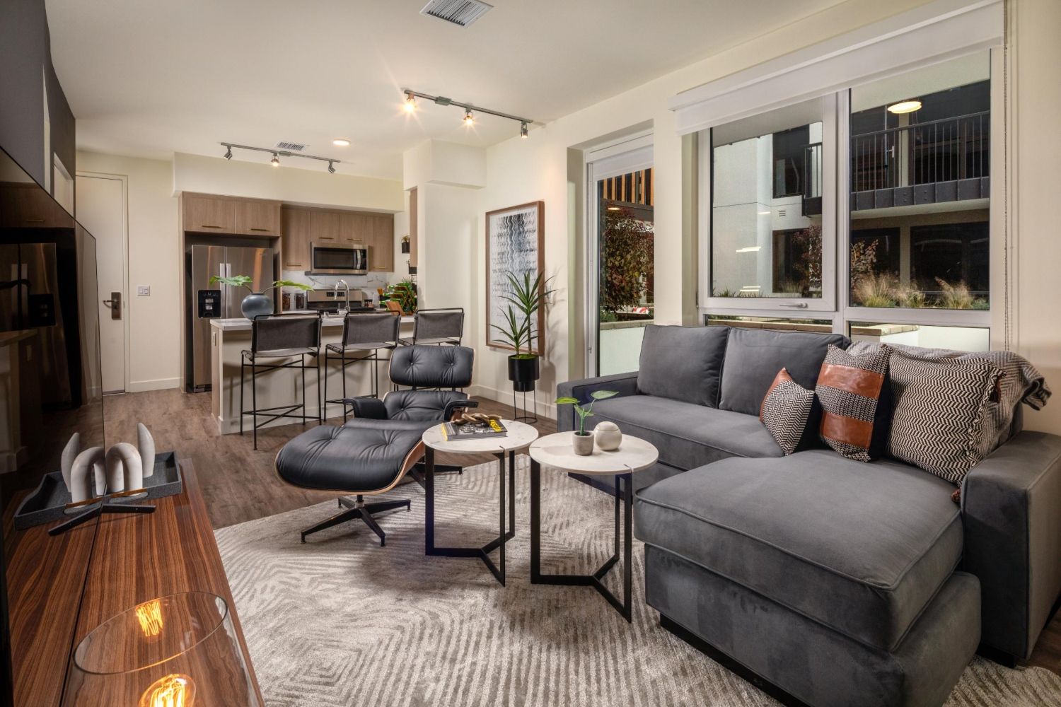 Modern living room with gray sofa, coffee tables, and kitchen in the background.