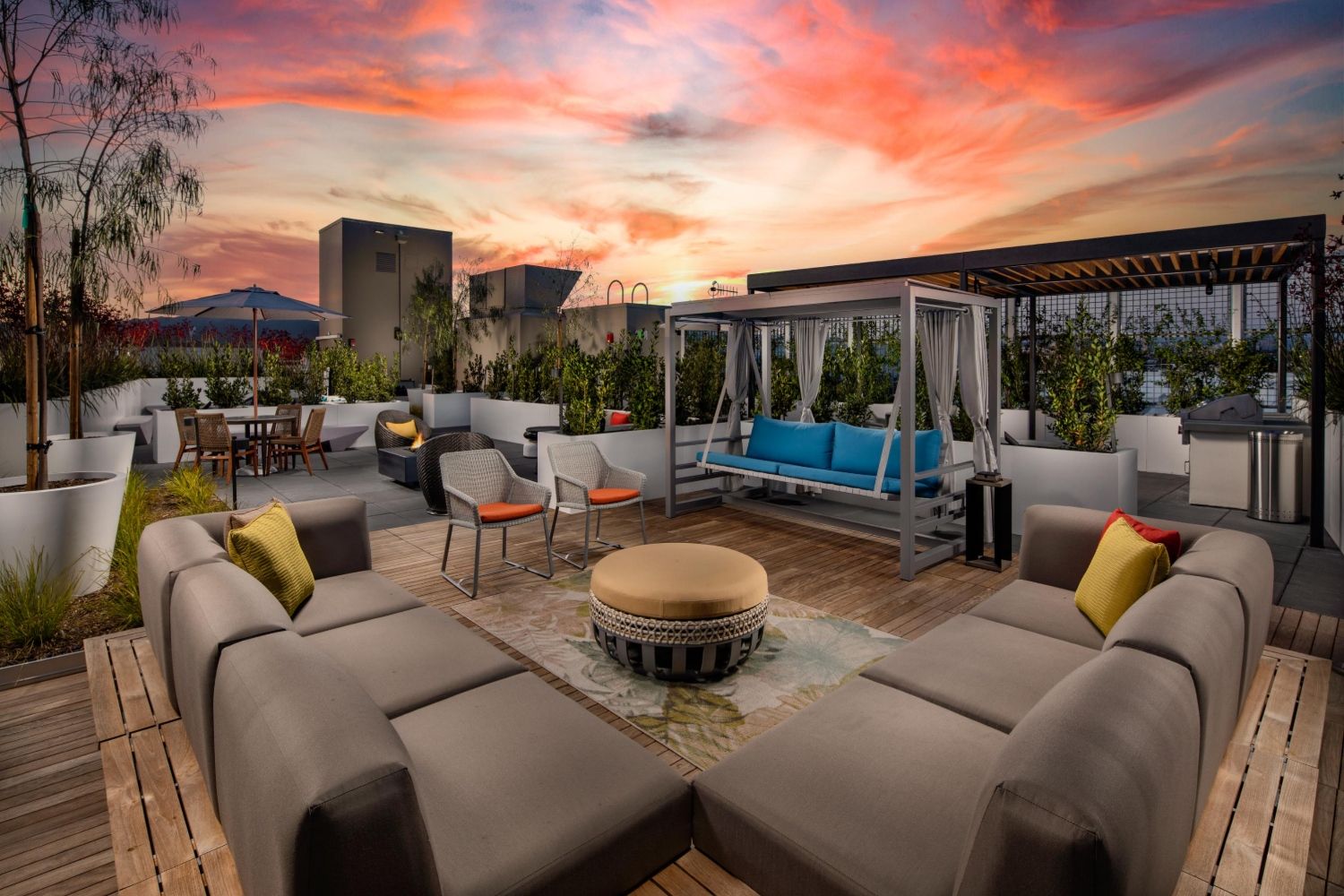 Modern rooftop lounge with cozy seating and a vibrant sunset backdrop.