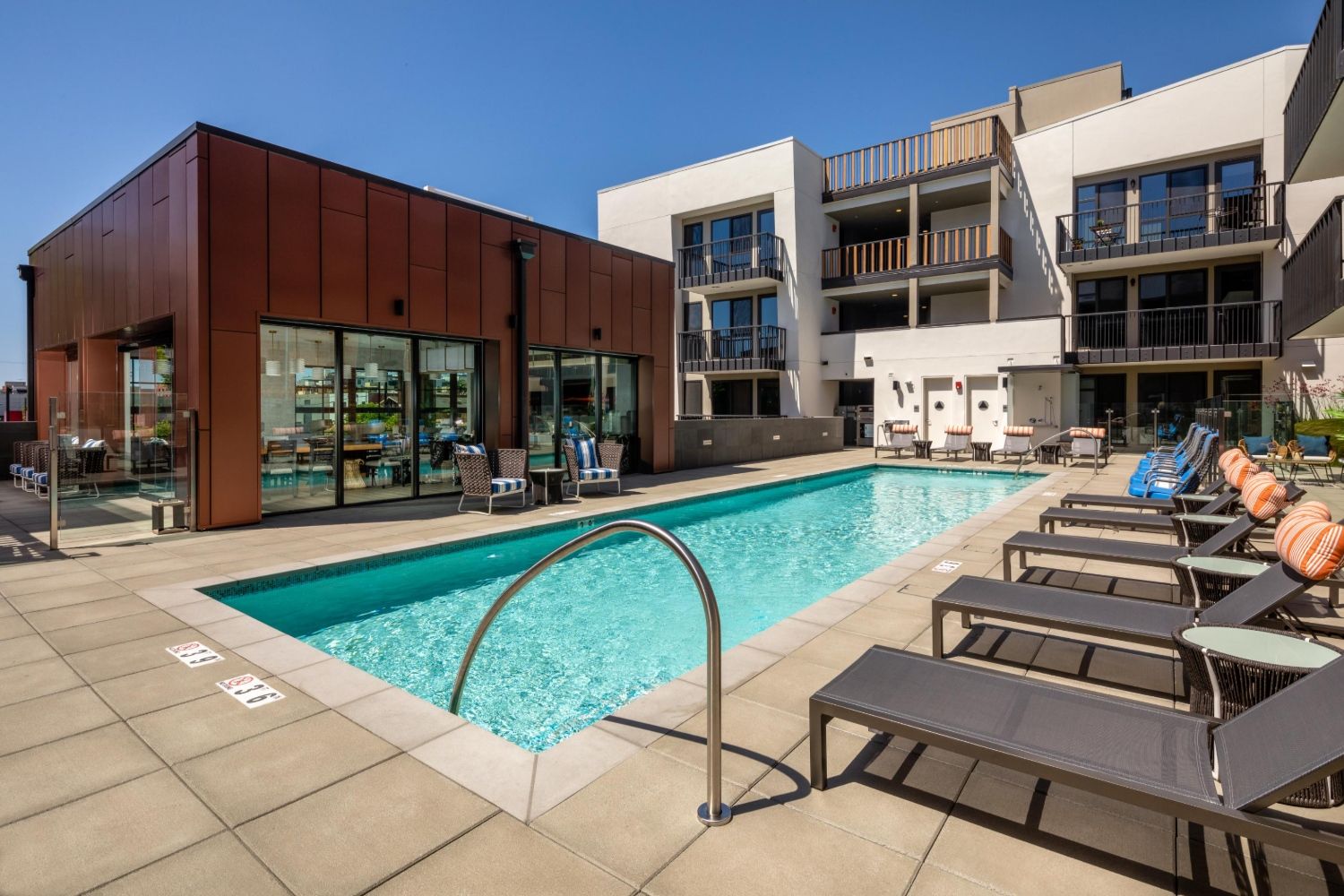Modern pool area with lounge chairs and surrounding apartment buildings on a sunny day.