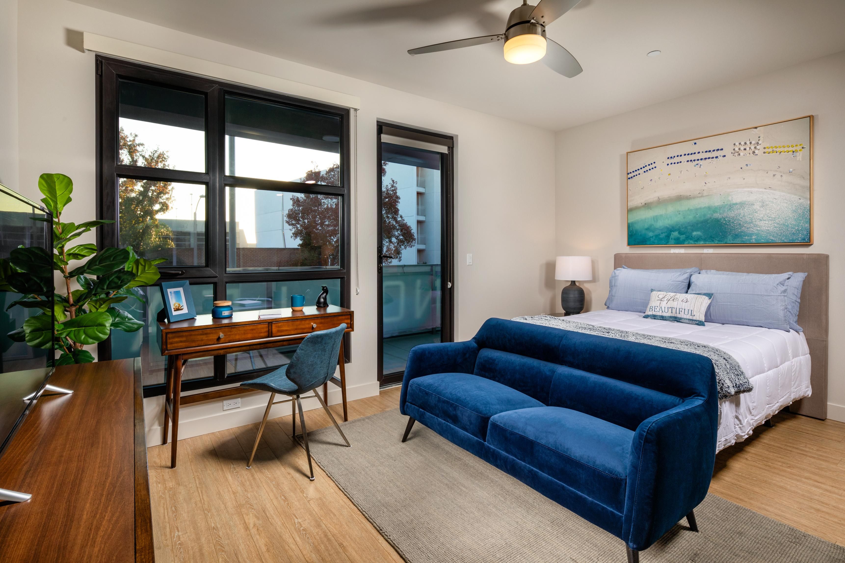 Modern bedroom featuring a blue sofa, desk, and large windows with natural light.