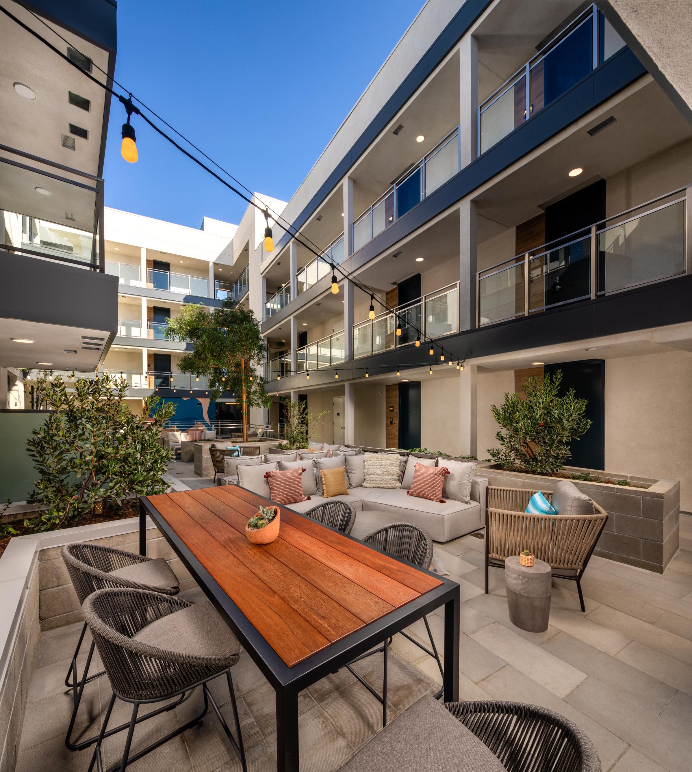Modern outdoor seating area with a wooden table and cozy chairs in a courtyard setting.