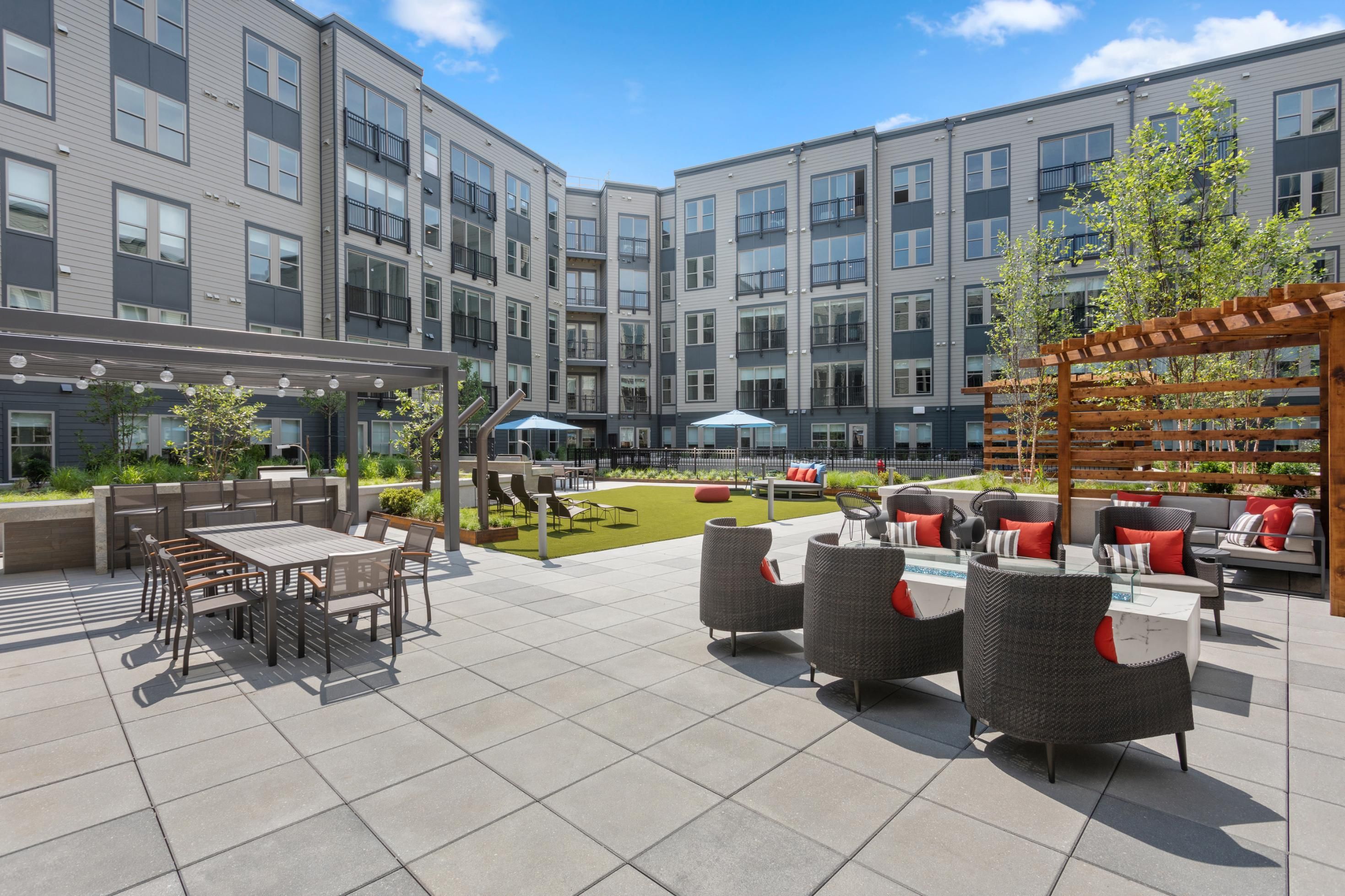 Modern outdoor patio with seating and greenery surrounded by apartment buildings.