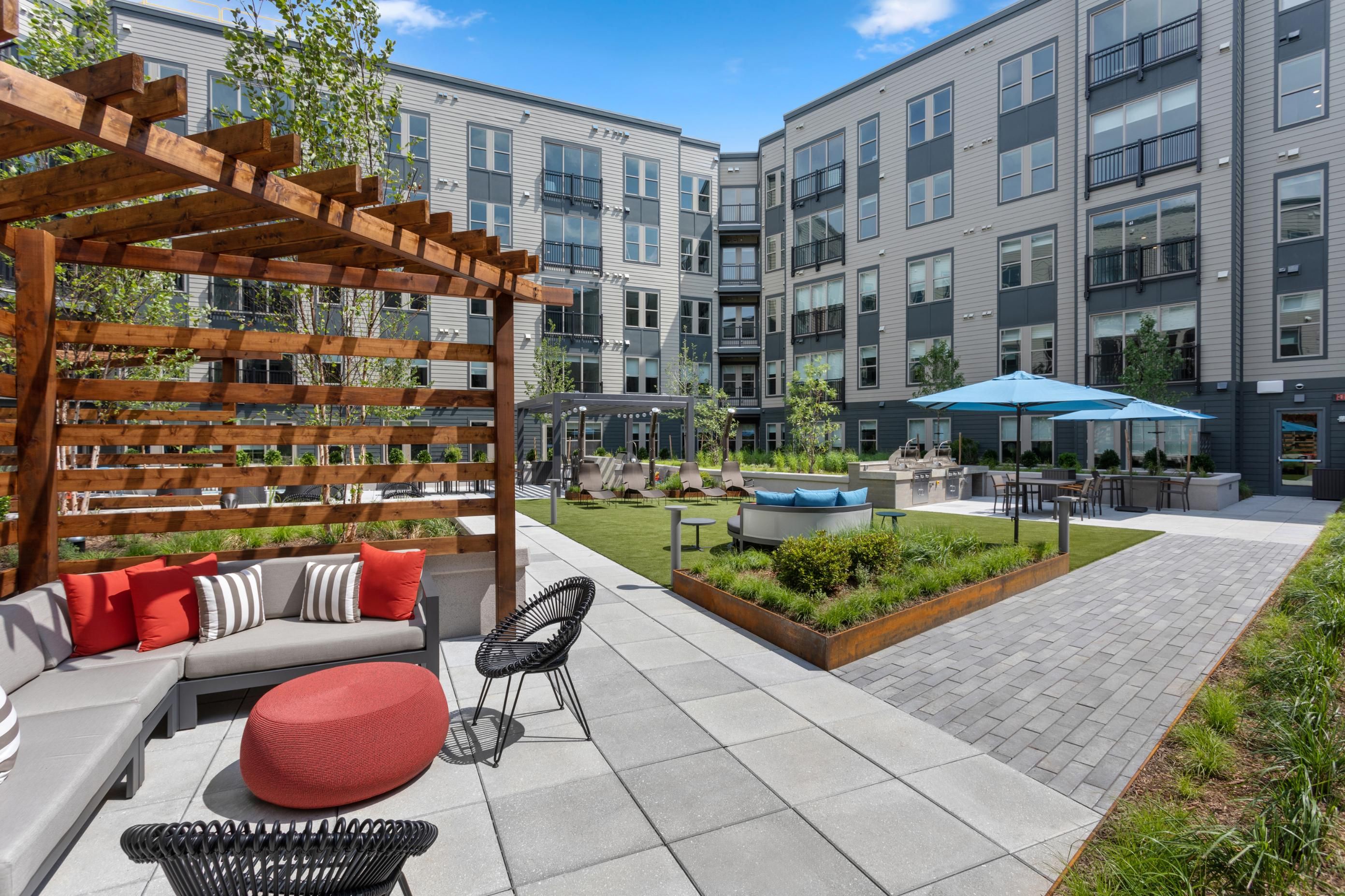 Modern outdoor patio area with seating, greenery, and a pool surrounded by apartment buildings.