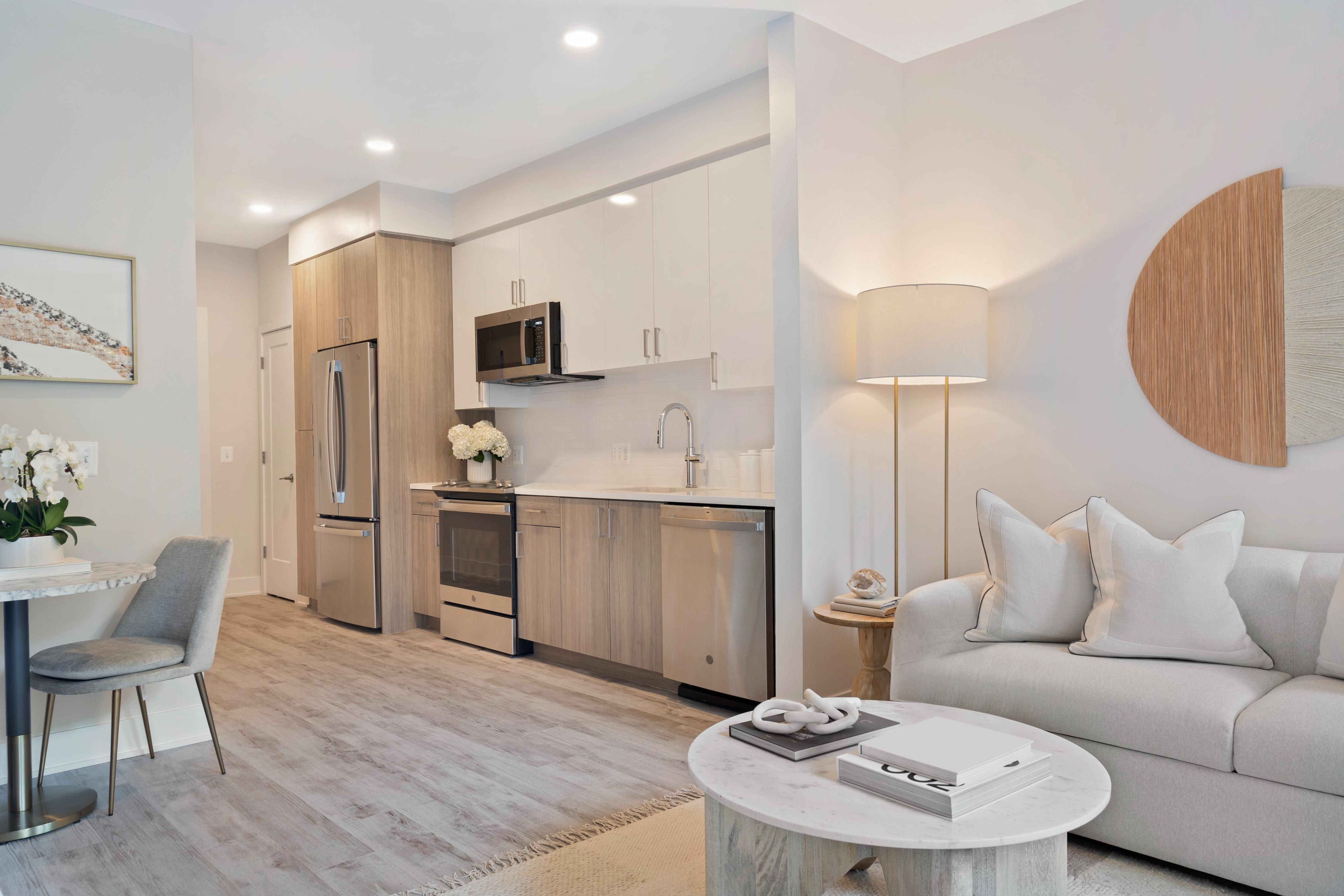 Modern, minimalist apartment interior featuring a kitchen and living area with neutral tones.