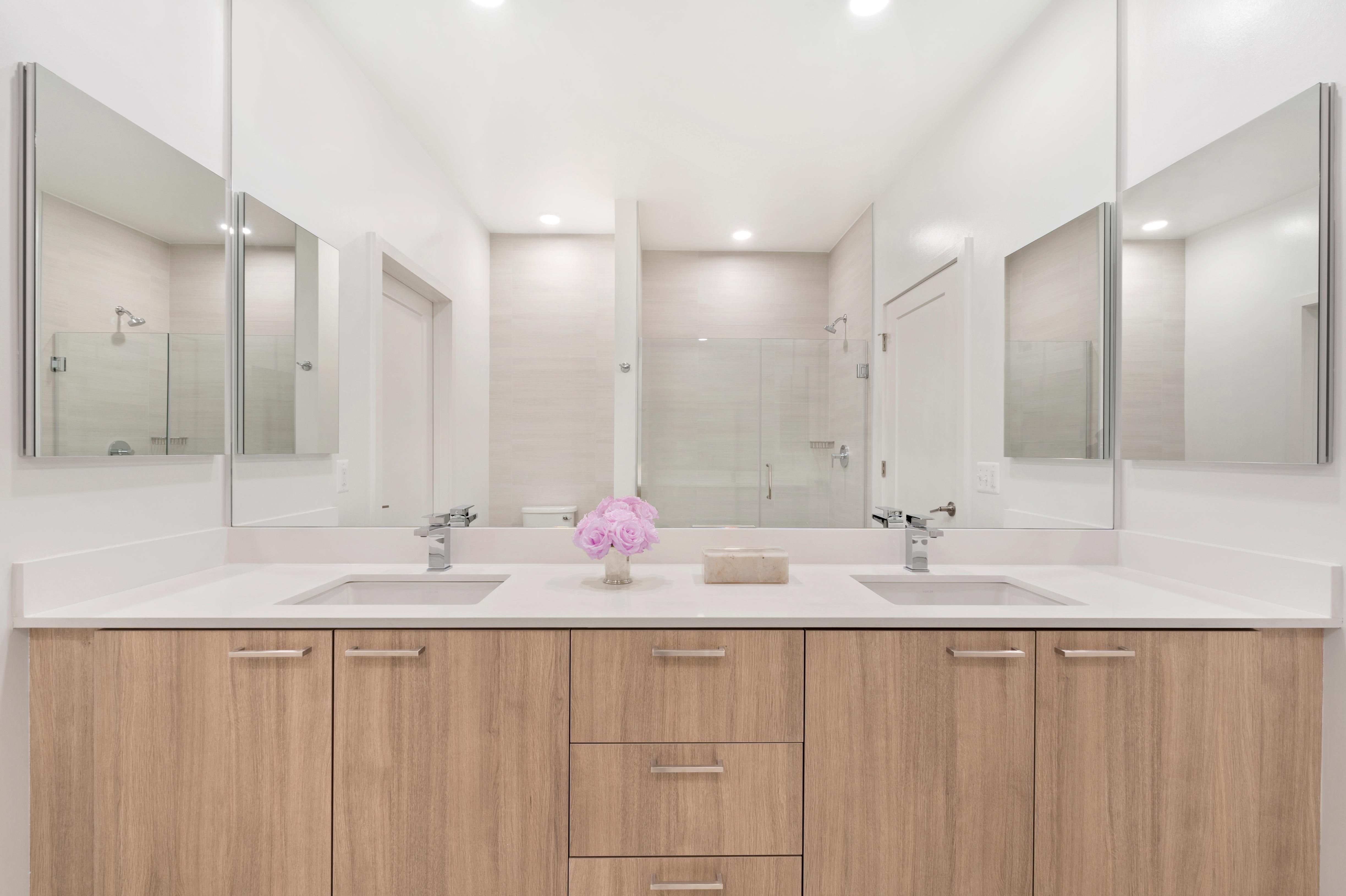 Modern bathroom with dual sinks, light wood cabinetry, and large mirrors.
