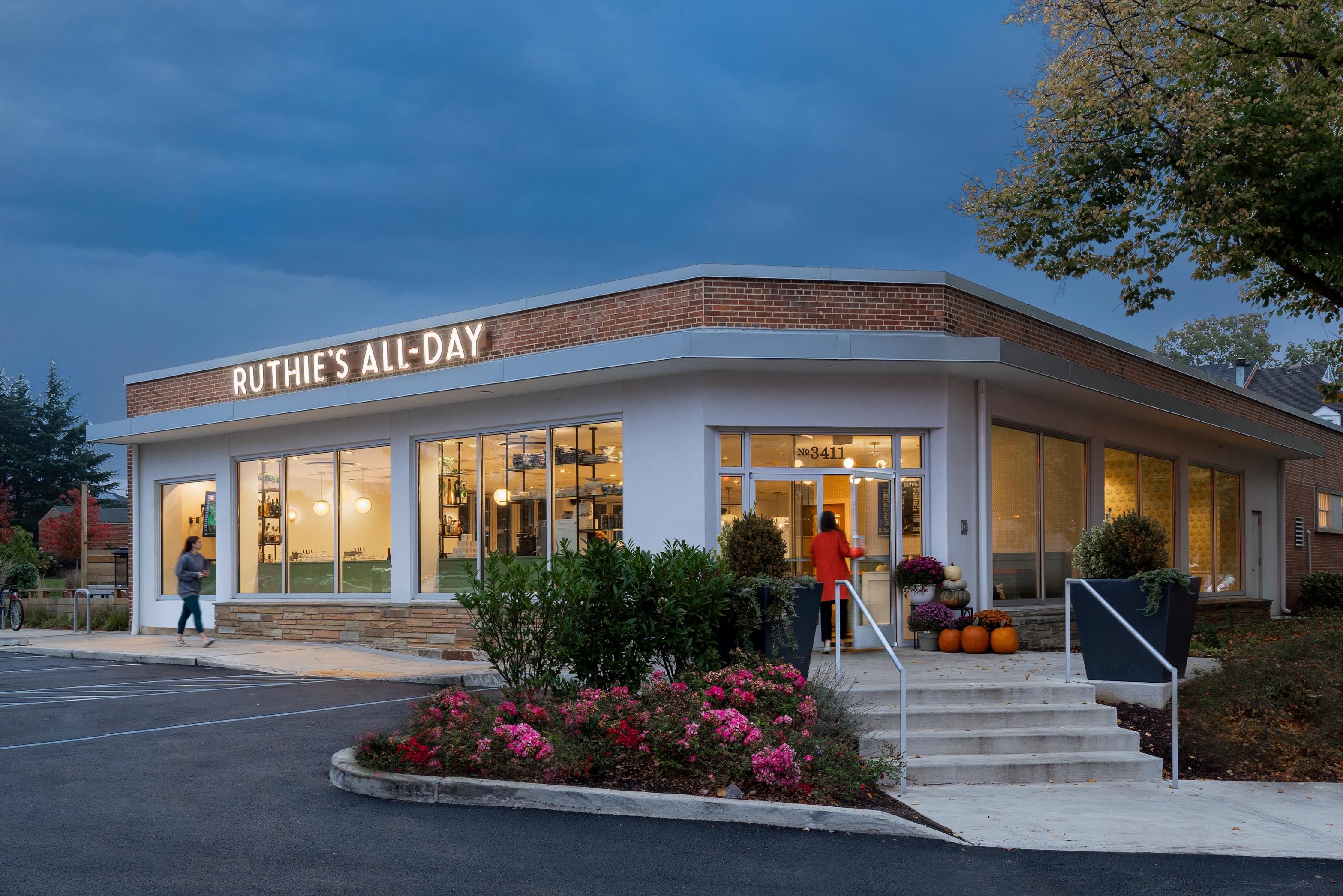 Modern restaurant exterior with large windows, outdoor seating, and autumn decorations.