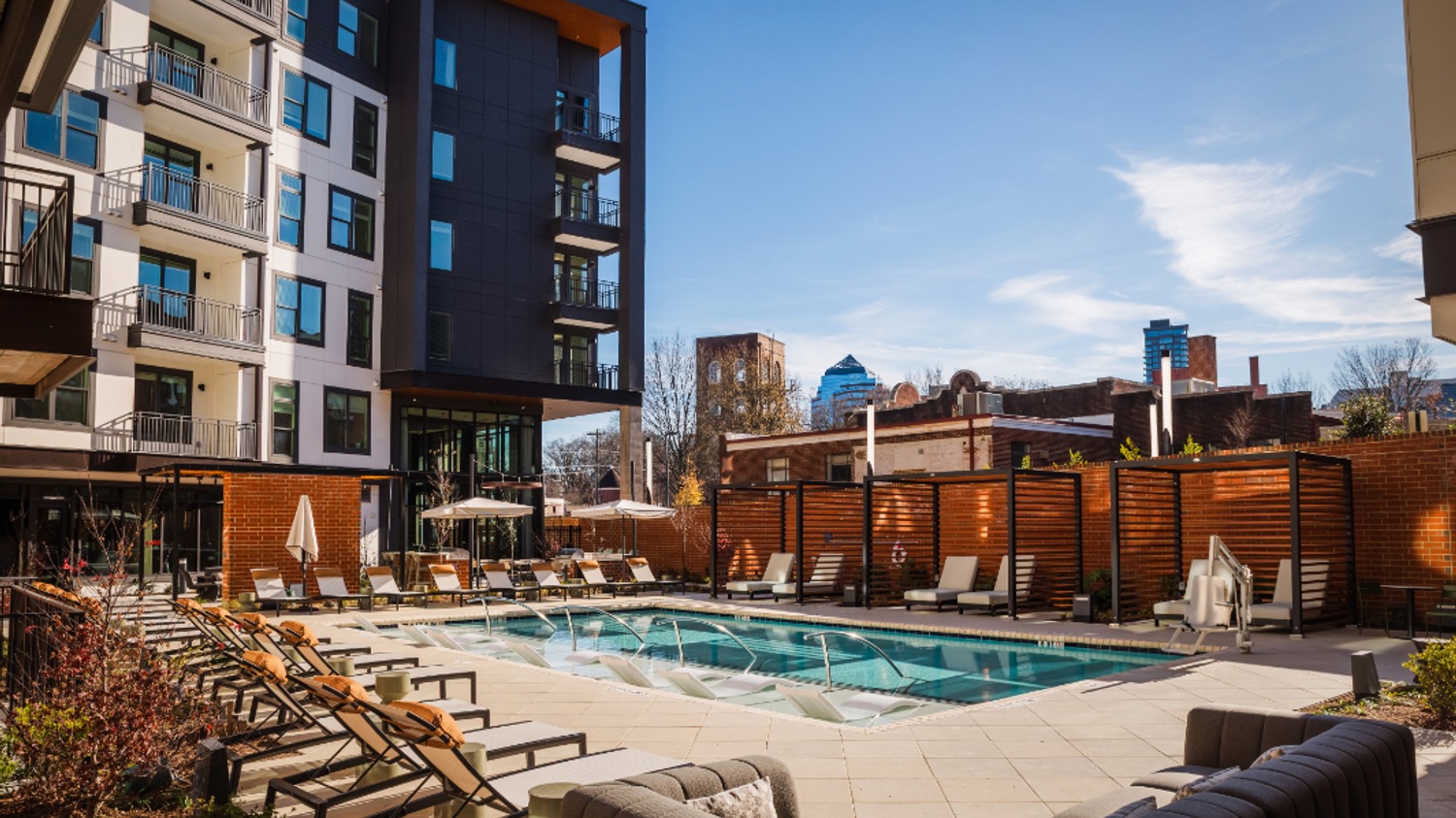A modern apartment complex with a pool and lounge chairs under a clear blue sky.