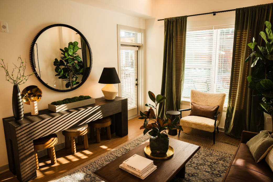 A stylish living room with green curtains, a mirror, and plants.