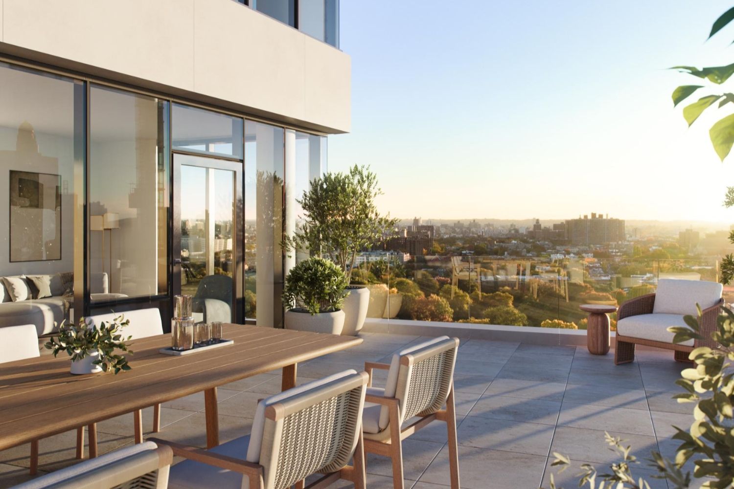 Modern patio with a dining table, chairs, and greenery, overlooking a sunset view.