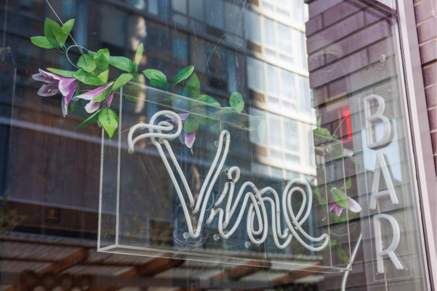 Sign for "Vine Bar" with floral design on a glass surface and modern building reflection.