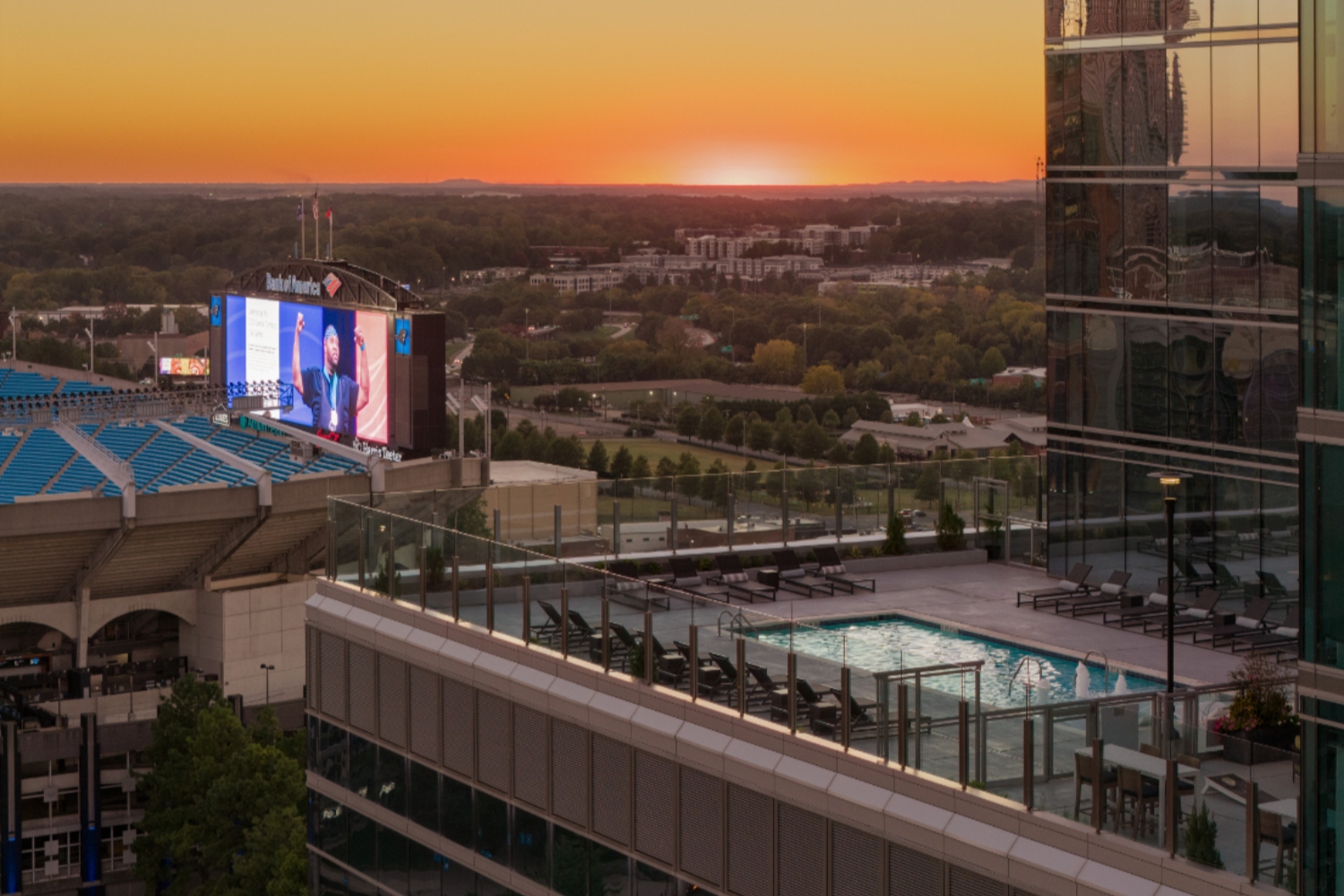 Sunset over a city skyline with a pool and large screen in view.
