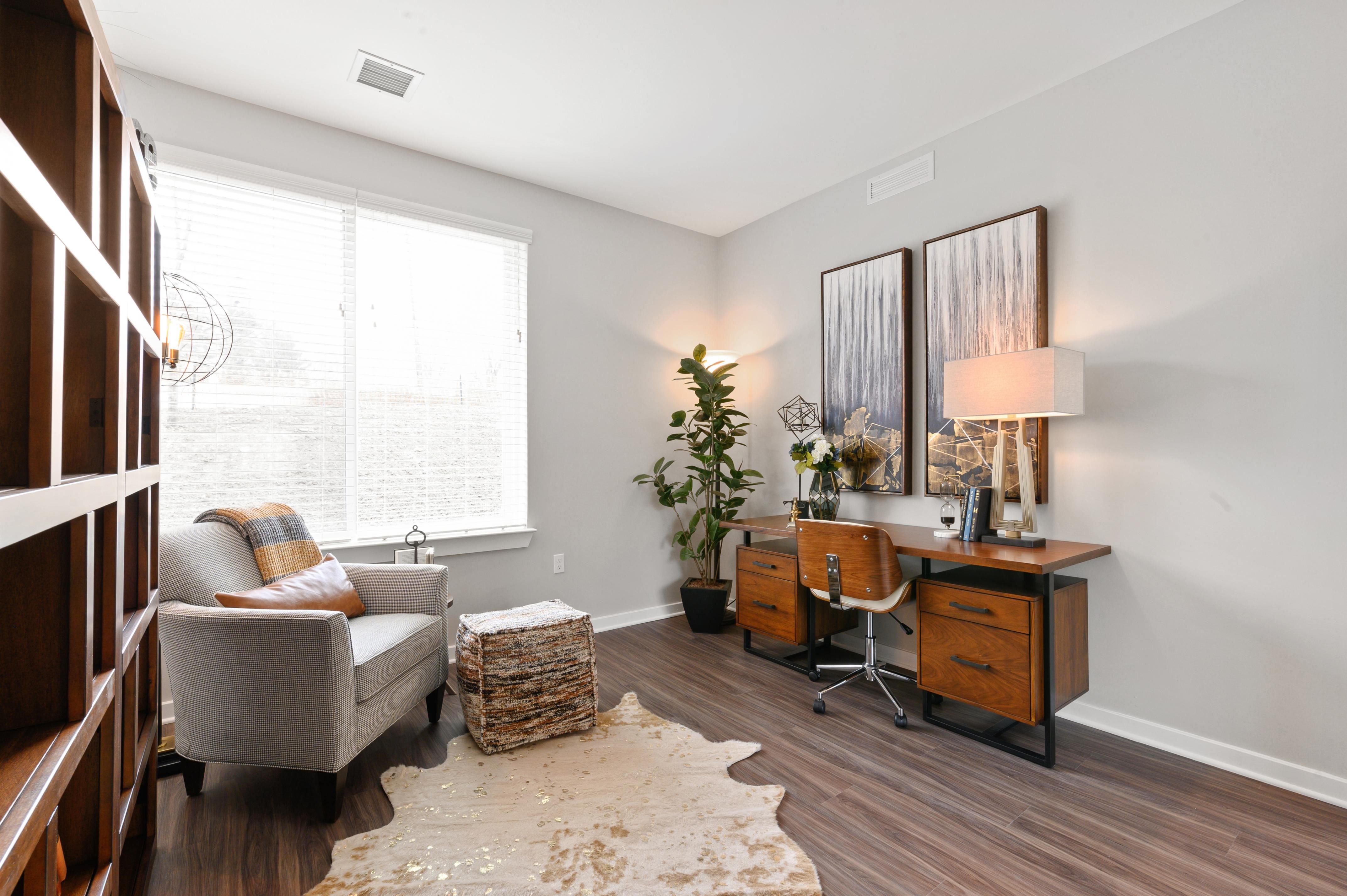 Cozy home office with a desk, armchair, and natural light from a large window.